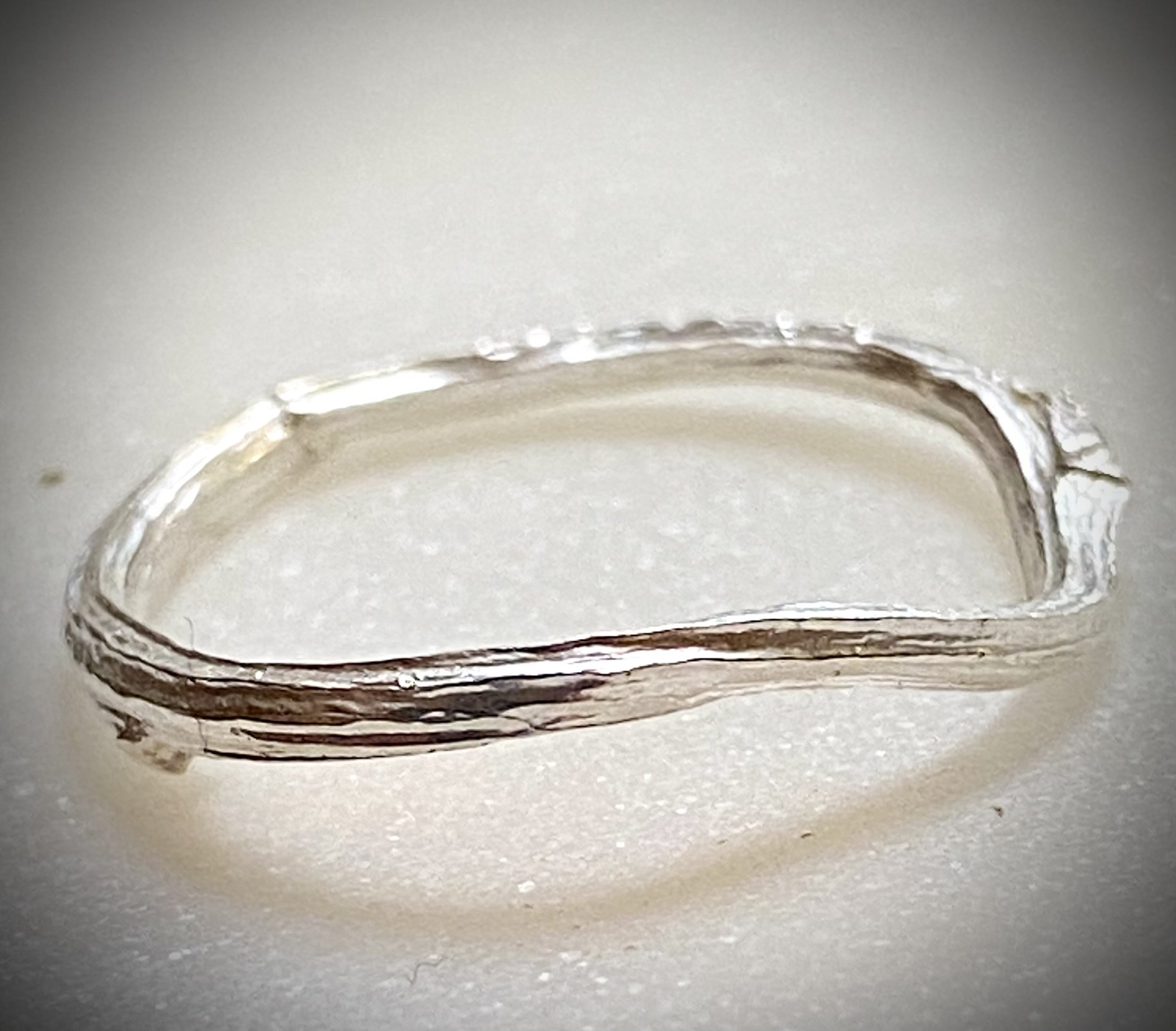 Close-up of a silver ring with a simple band design on a light-colored background.