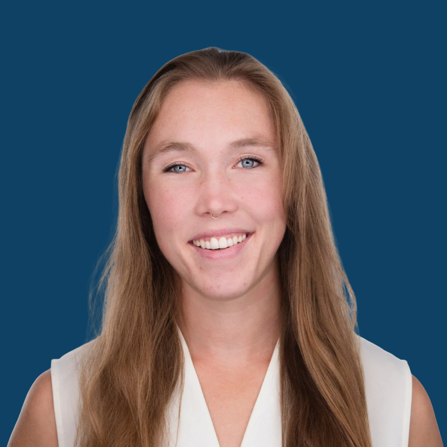 A woman with long, light brown hair and blue eyes smiling, wearing a white sleeveless top, against a solid dark blue background.