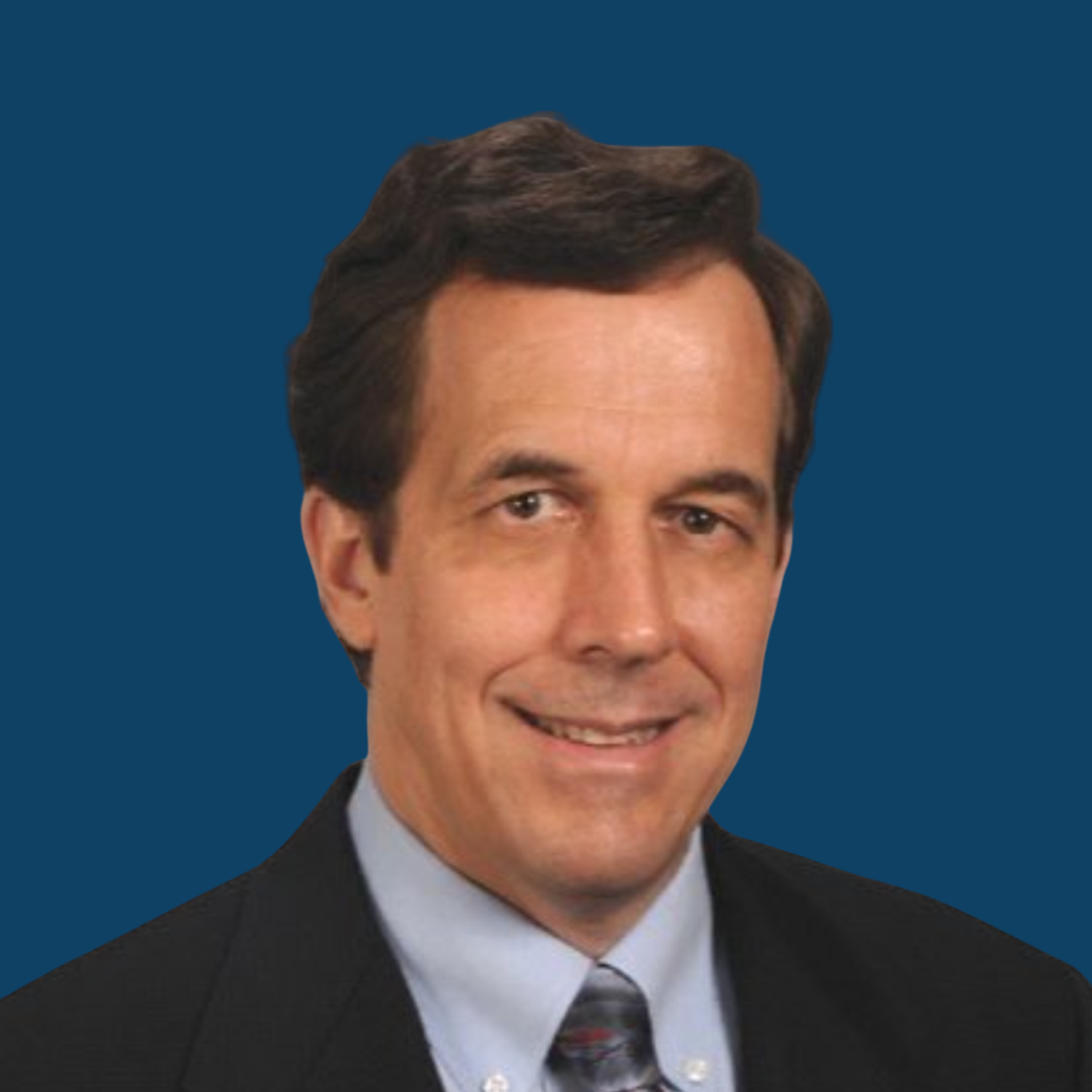 Headshot of a man with dark hair wearing a suit and tie against a dark blue background.
