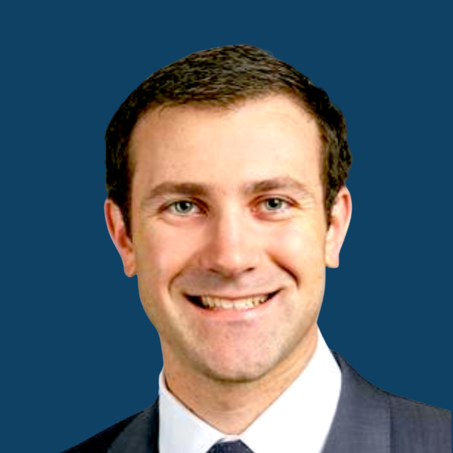 Portrait of a smiling man wearing a suit and tie against a solid blue background.