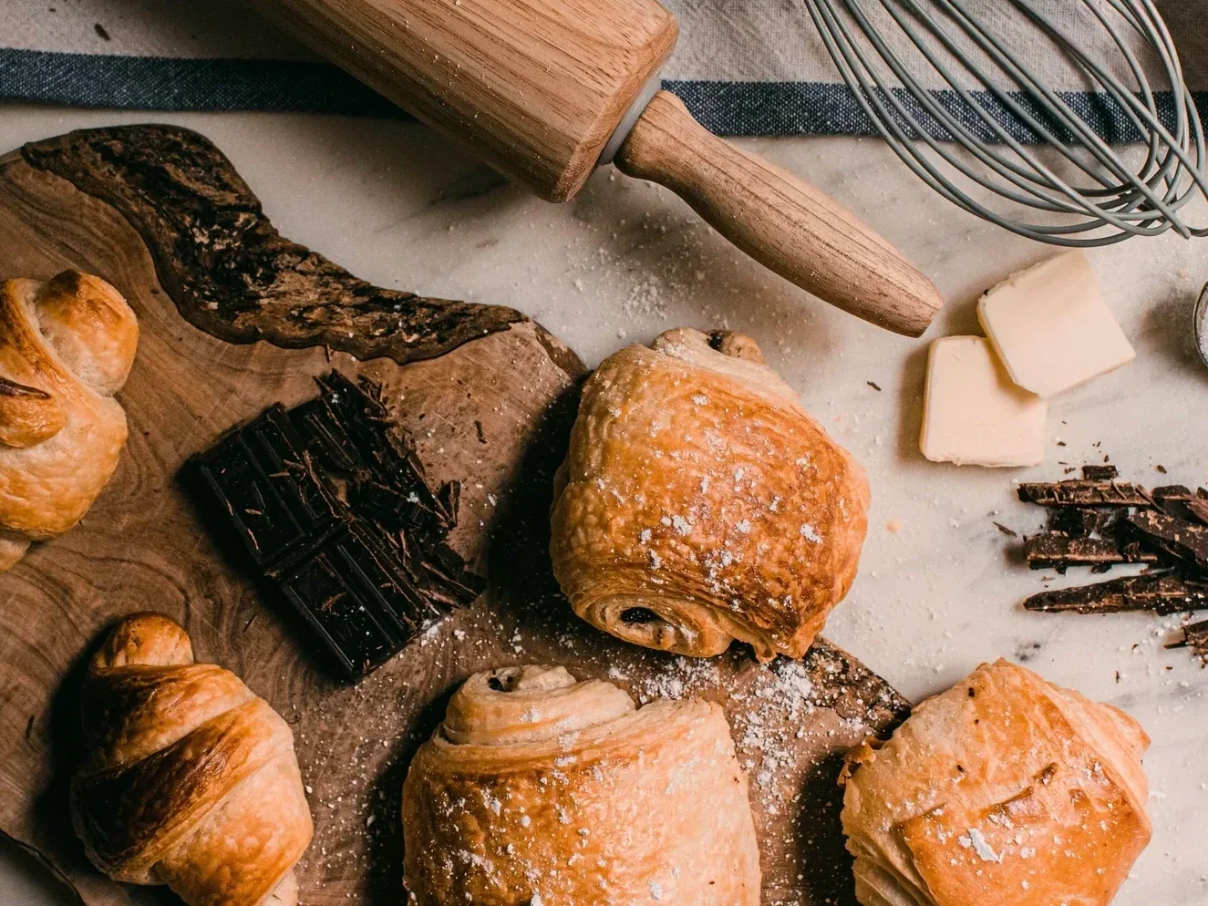 Photo of various pastries, a rolling pin, a whisk, and some butter.