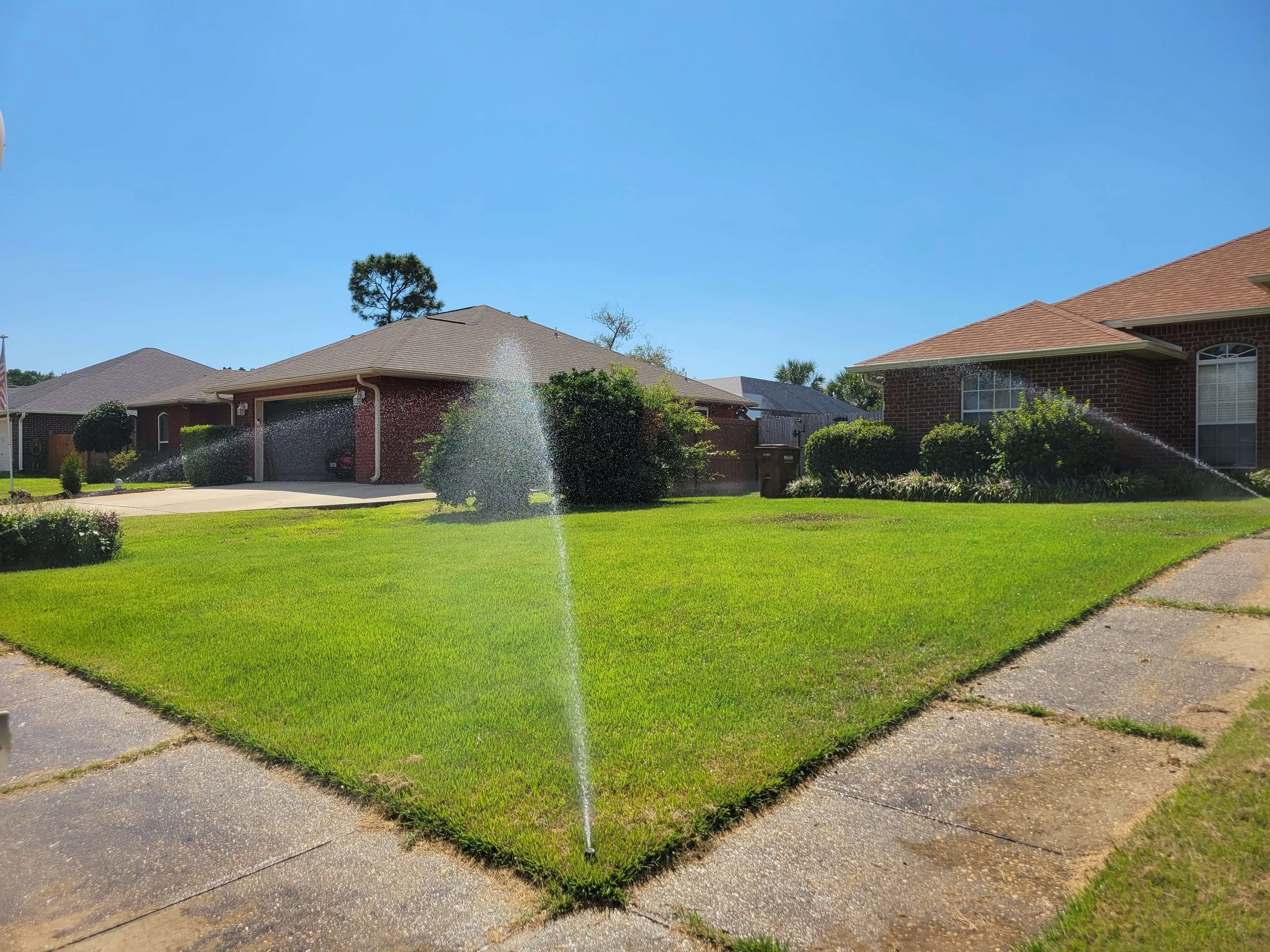 Front lawn of a suburban house with a sprinkler watering the grass on a sunny day.