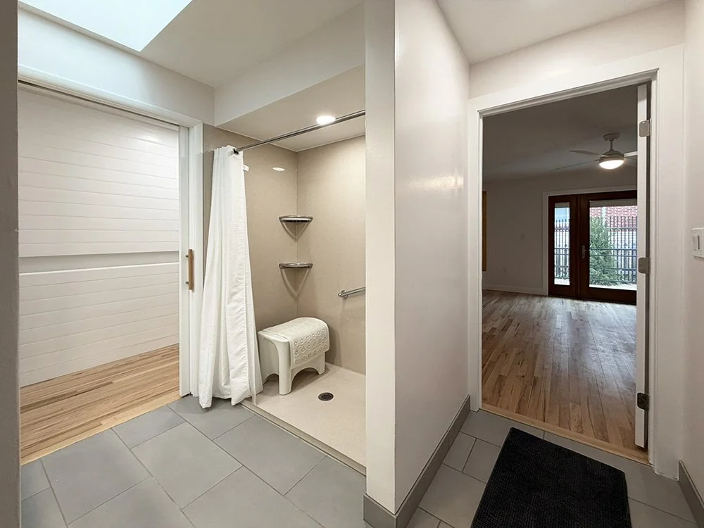 The roll-in shower in the main bathroom. One door leads to the hall. A secondary door leads to the primary suite bedroom.