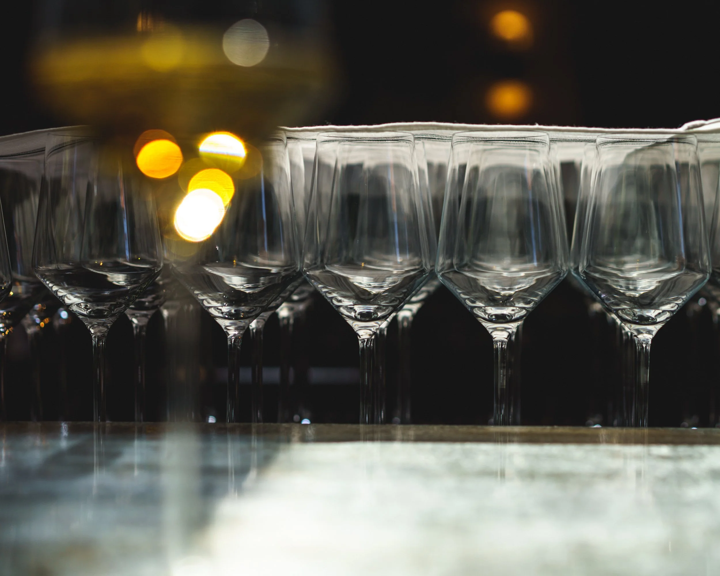 Row of empty wine glasses on a bar counter with blurred city lights in the background.