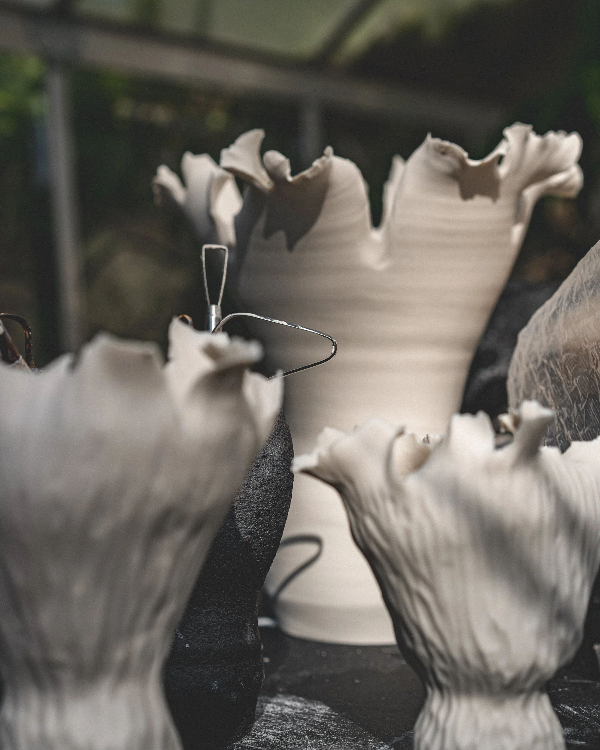 Close-up of ceramic vases with ruffled edges, arranged on a surface with some metal jewelry in front.