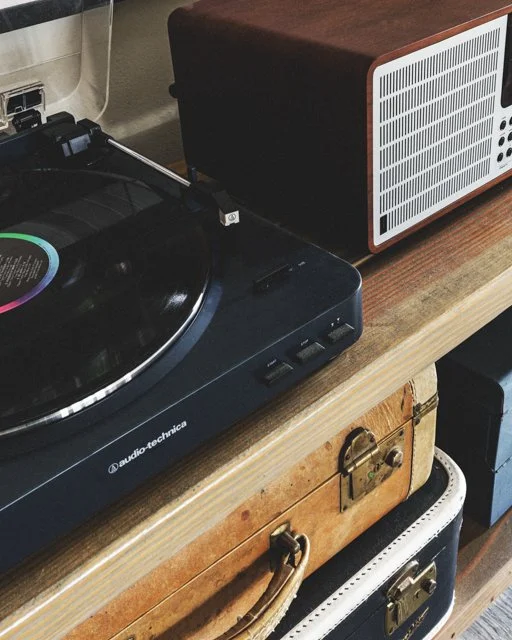 A turntable, speaker, and suitcases on a wooden table.