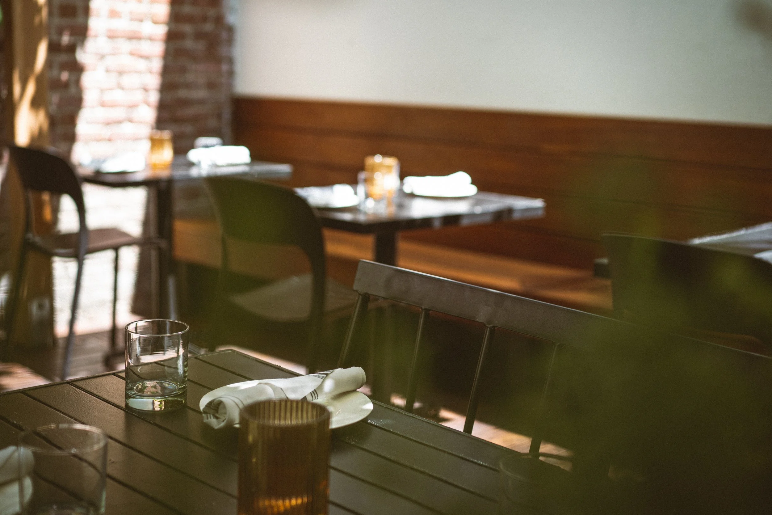Empty tables with folded napkins, glasses, and cutlery inside a restaurant with brick walls and wooden accents.