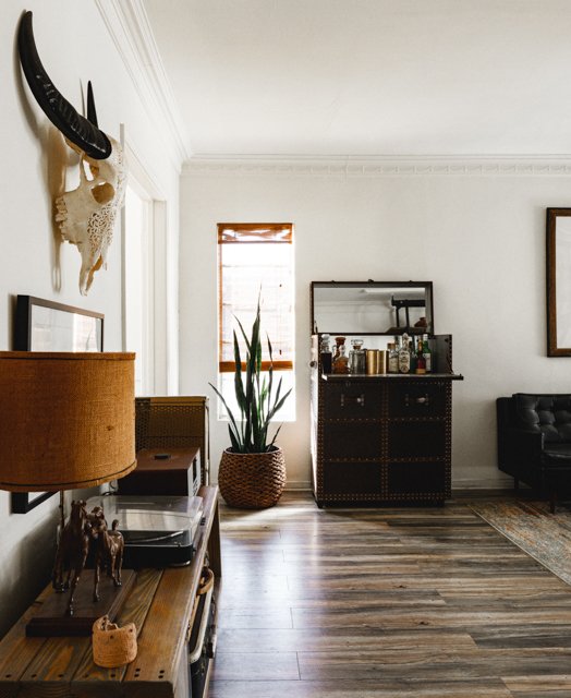 Living room with white walls, hardwood floor, a black bar cabinet, a potted plant, a window, and a piece of wall art.