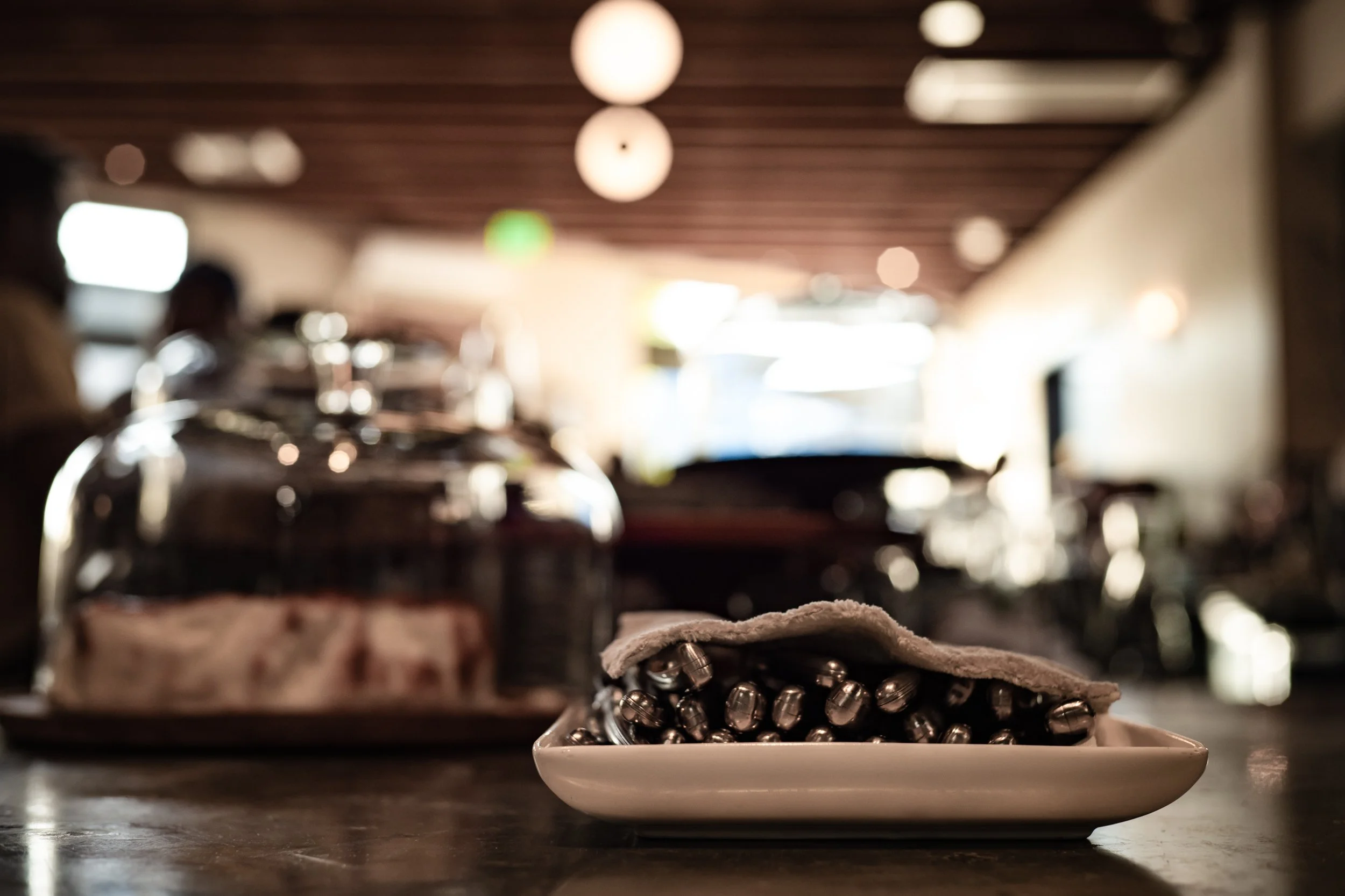 A plate of metallic capsules, possibly vitamins or supplements, on a table in a dimly lit café or restaurant. In the background, there are people and blurred lights.