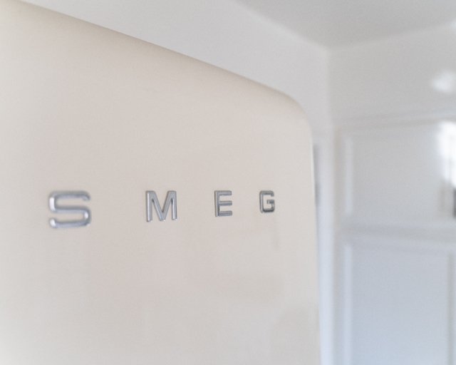 Close-up of a vintage Smeg refrigerator with metal letters spelling out 'SMEG' on a light-colored wall.