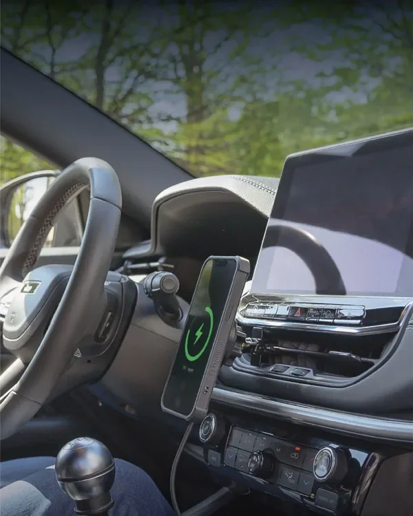 車の内部、運転席とハンドル、スマートフォンの充電中の充電器と画面表示、有線接続、ダッシュボードと空調コントロールパネル、外の風景が見える