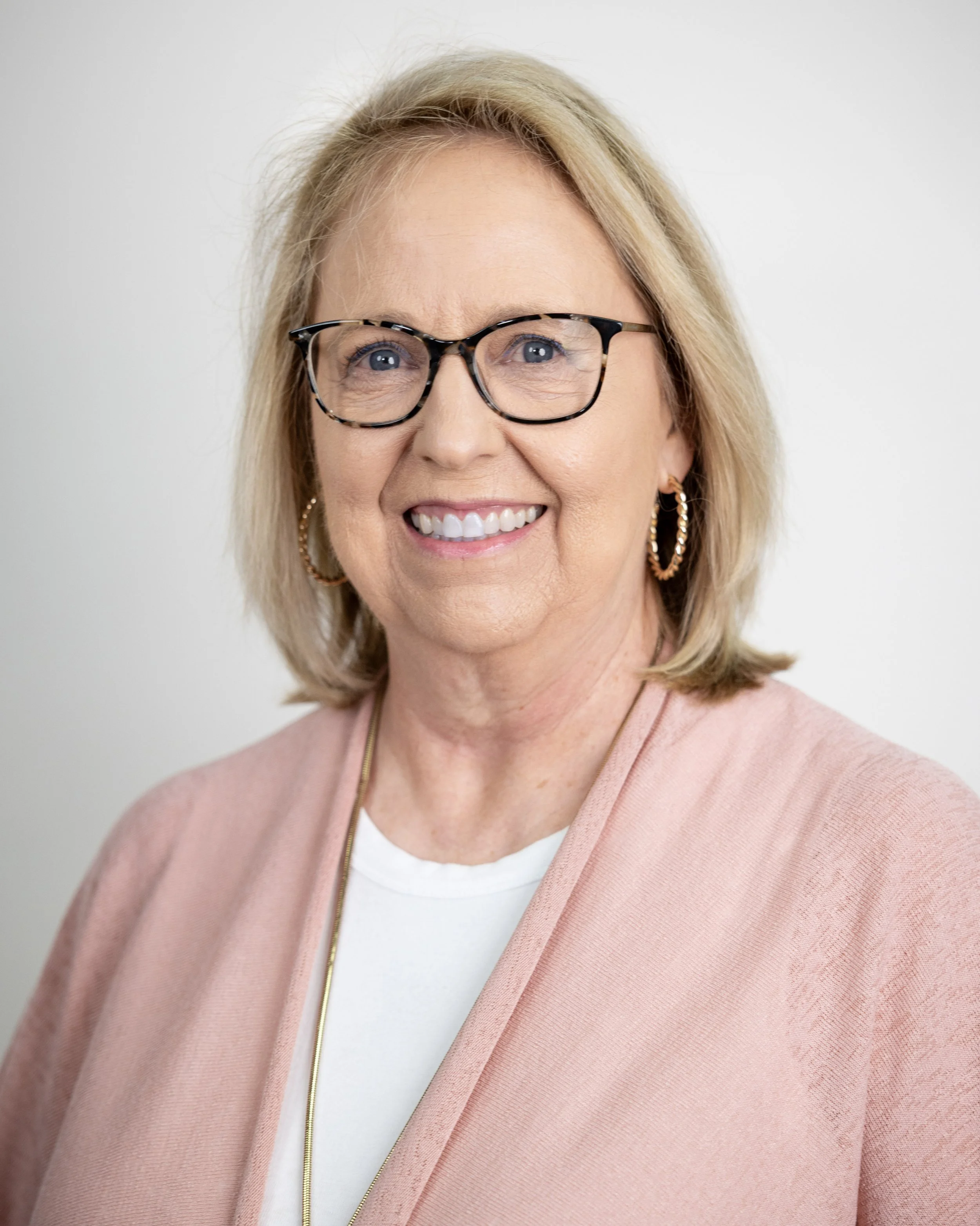 Smiling woman with glasses wearing a patterned shawl and necklace.