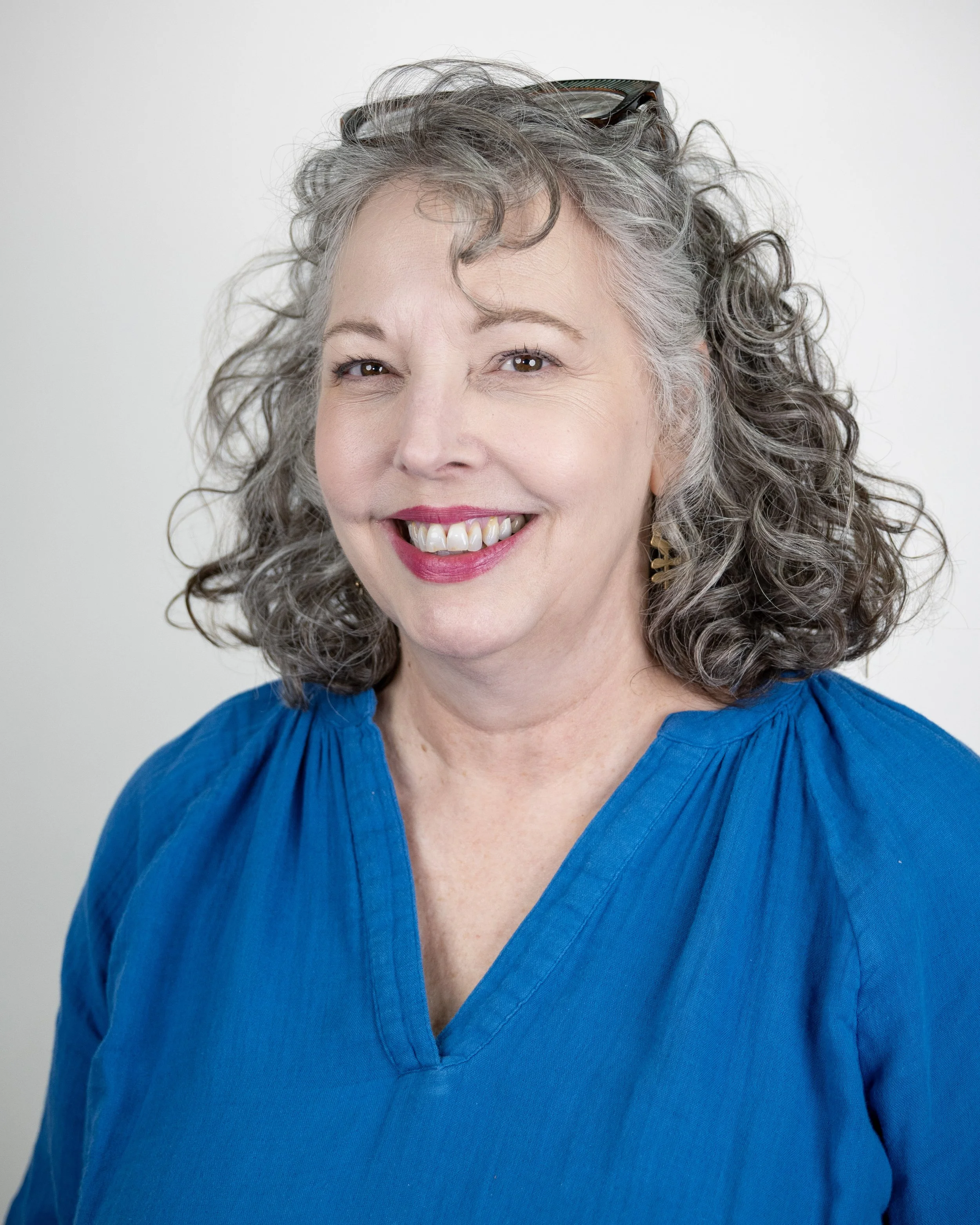 Smiling woman with gray curly hair wearing a white shirt.
