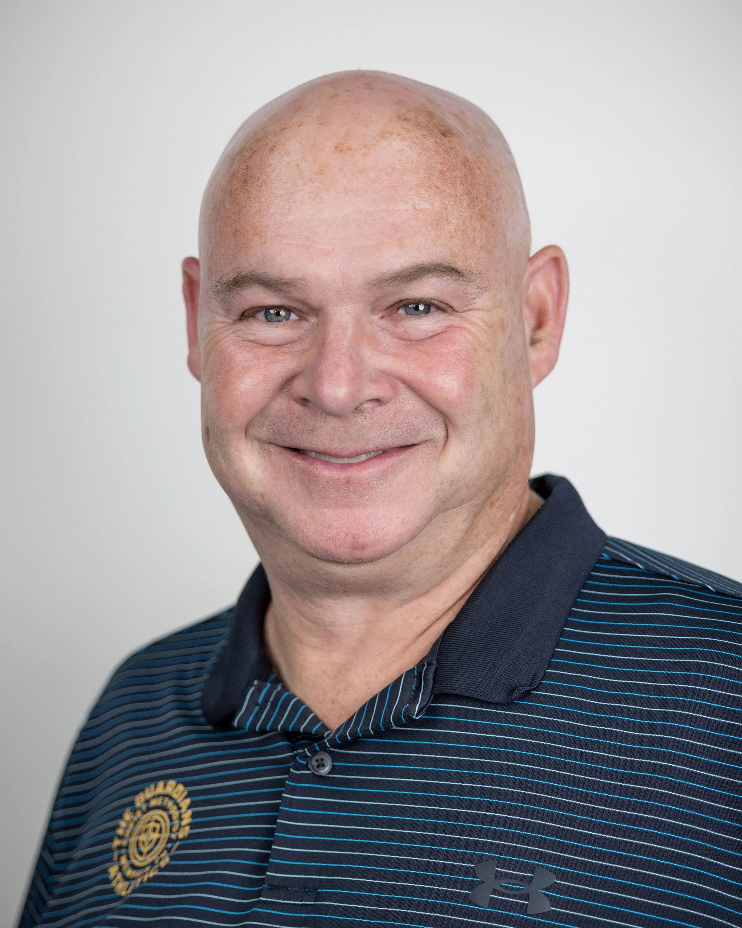 Bald man smiling in a plaid shirt against a plain background.