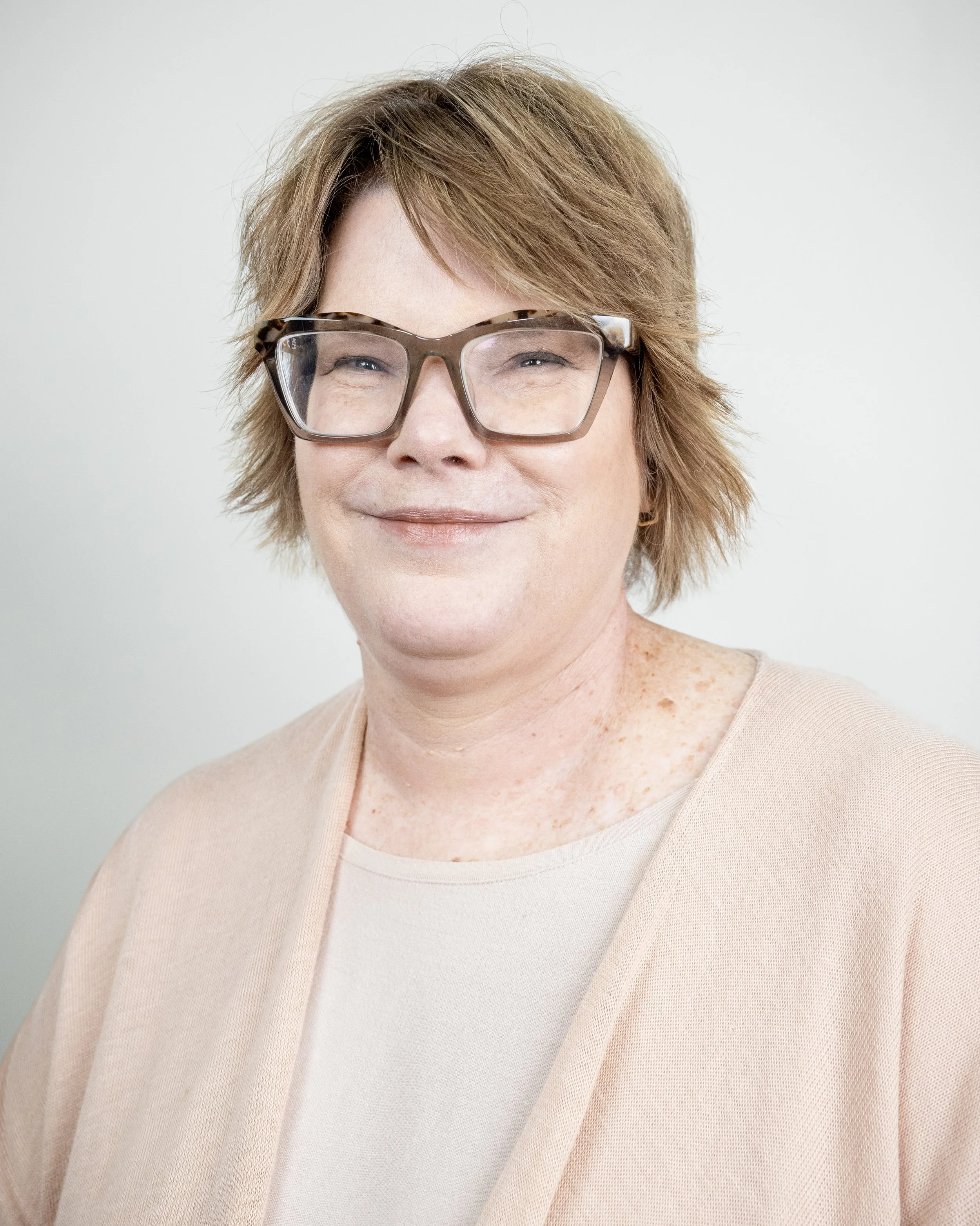 Smiling person with short brown hair and glasses, wearing a black hoodie and gray shirt.