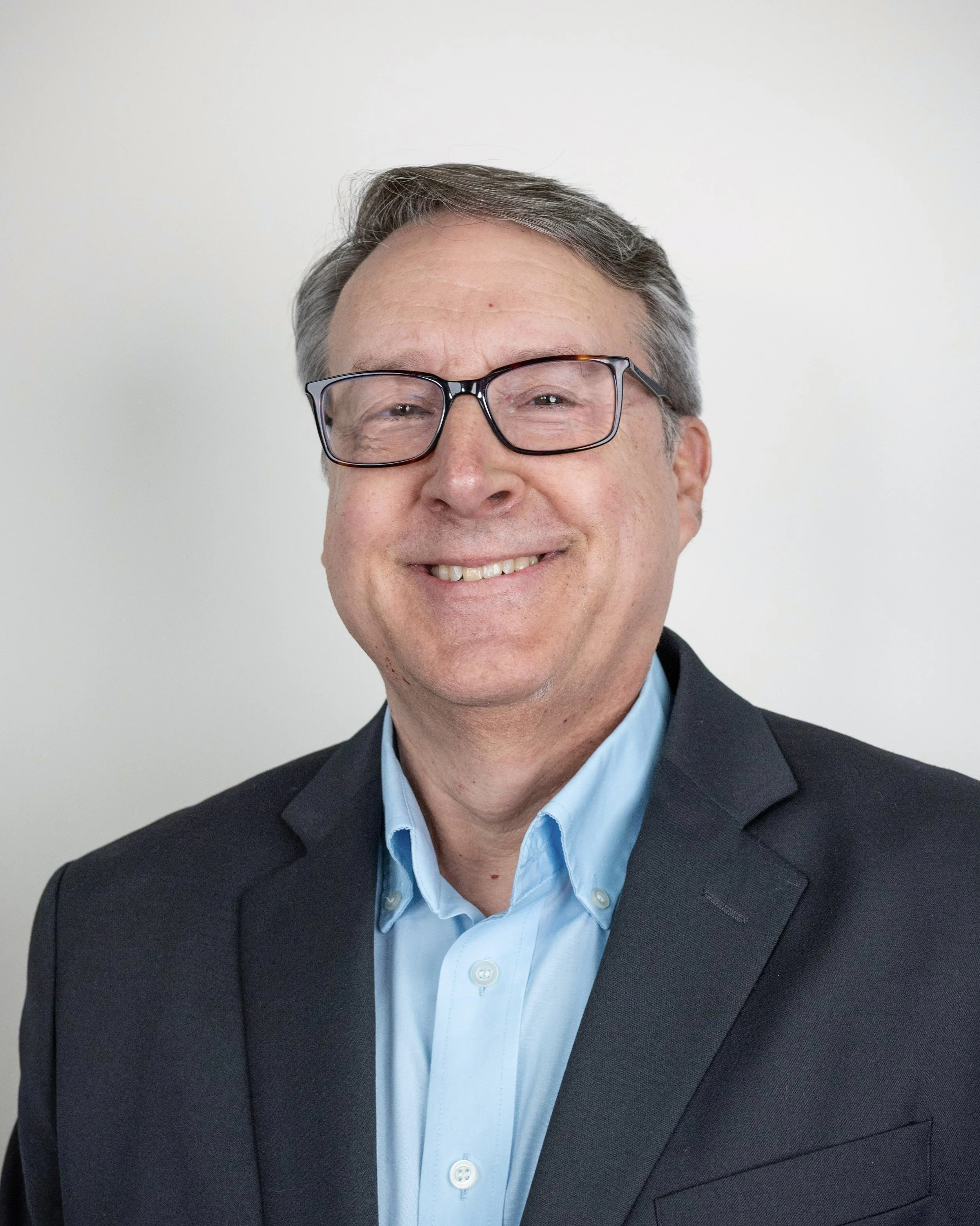 Smiling person wearing glasses and a suit jacket with a white shirt.