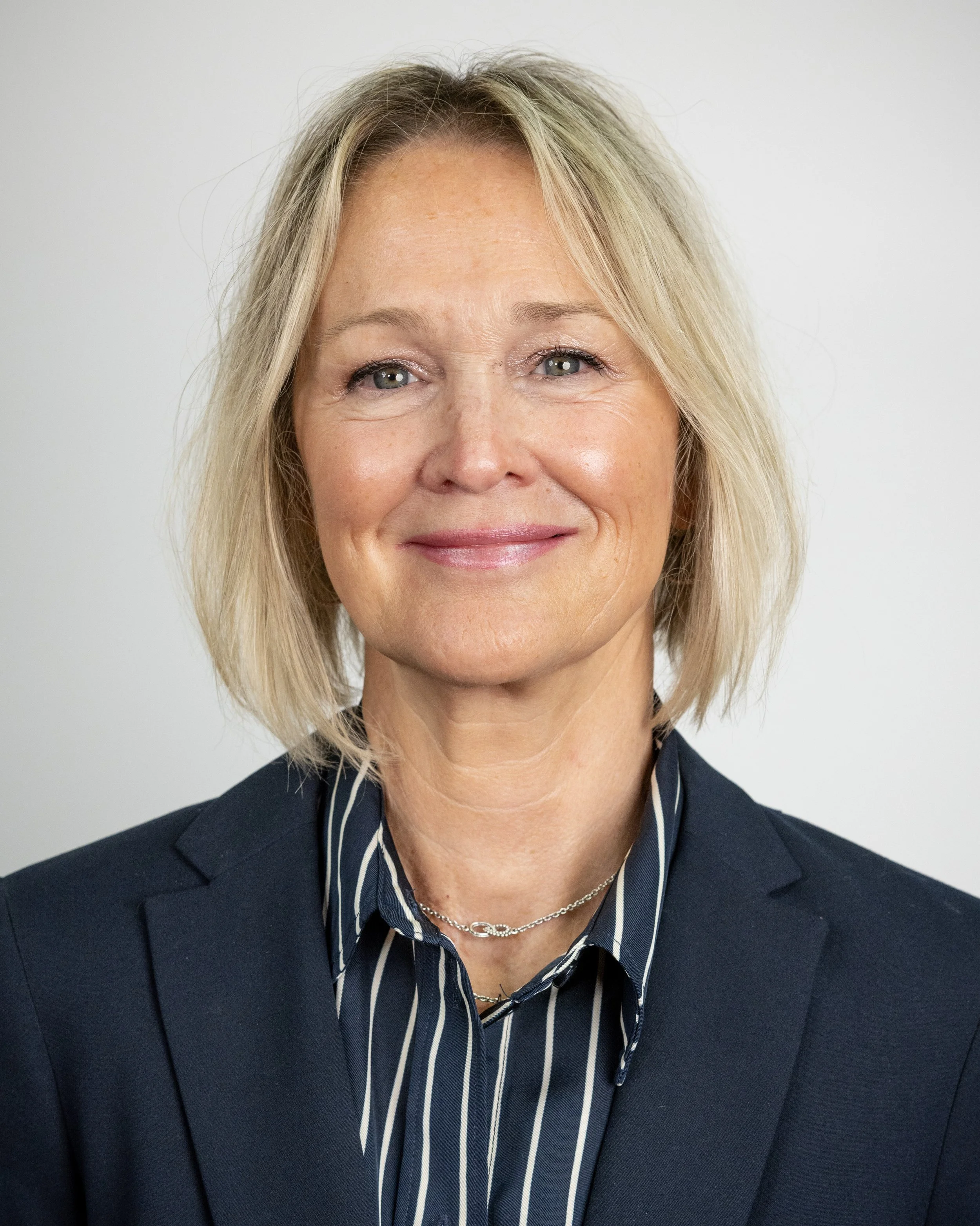 Portrait of a smiling person with short blonde hair, wearing a teal blouse and cardigan.