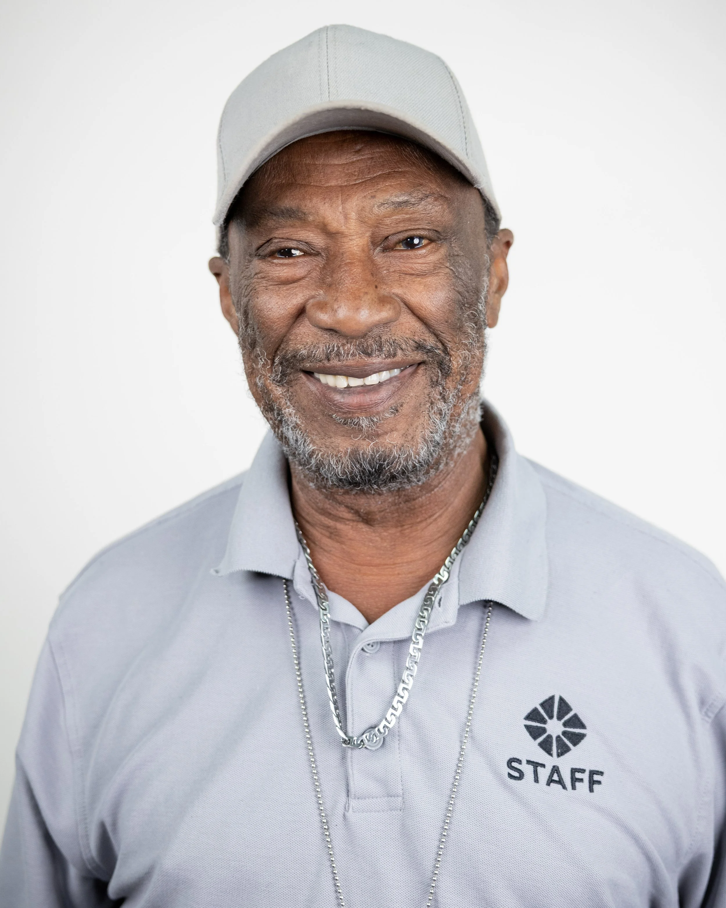 Smiling man wearing a light blue cap and collared shirt against a blue textured background.
