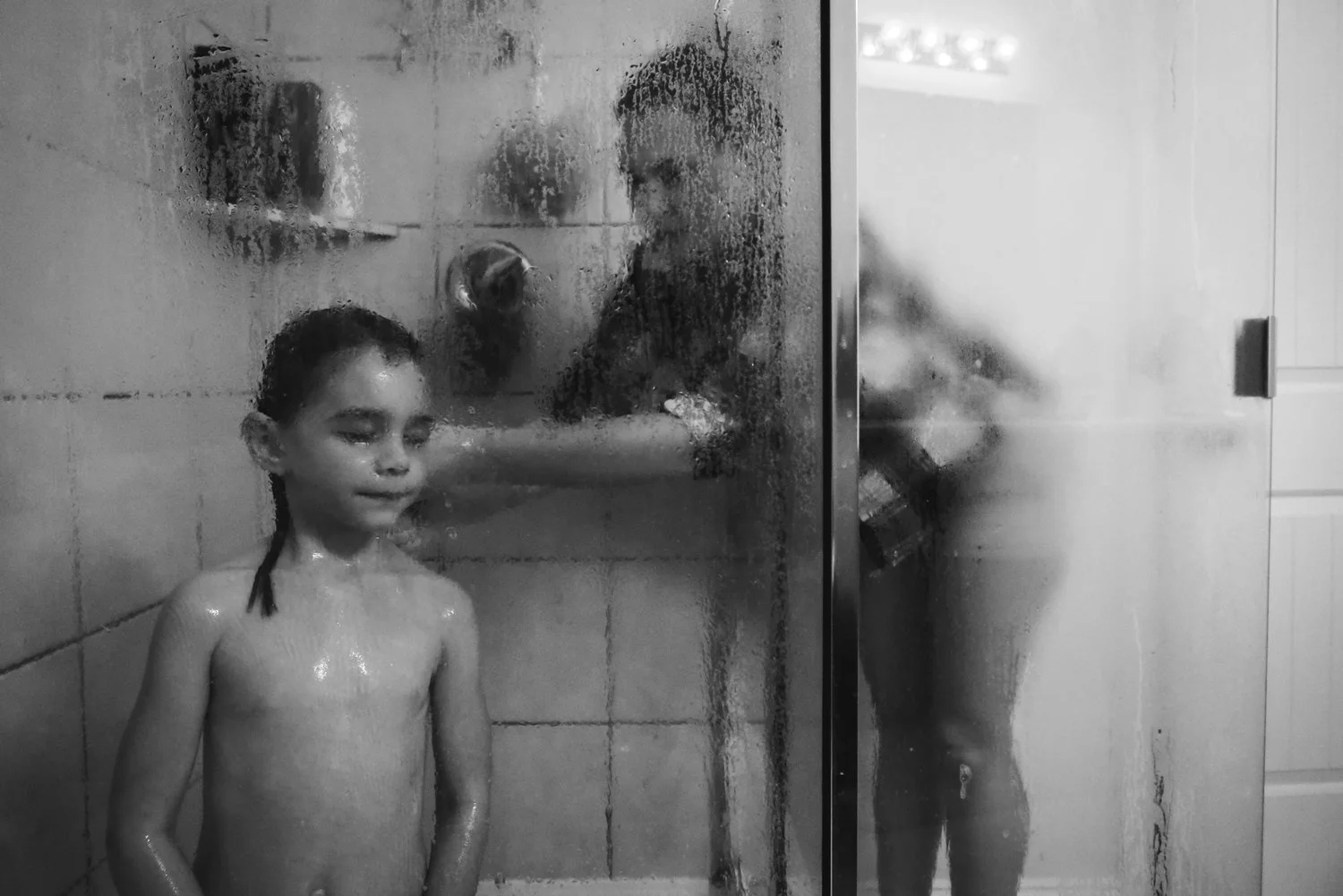 black and white photo of mom helping young daughter wash her hair in the shower