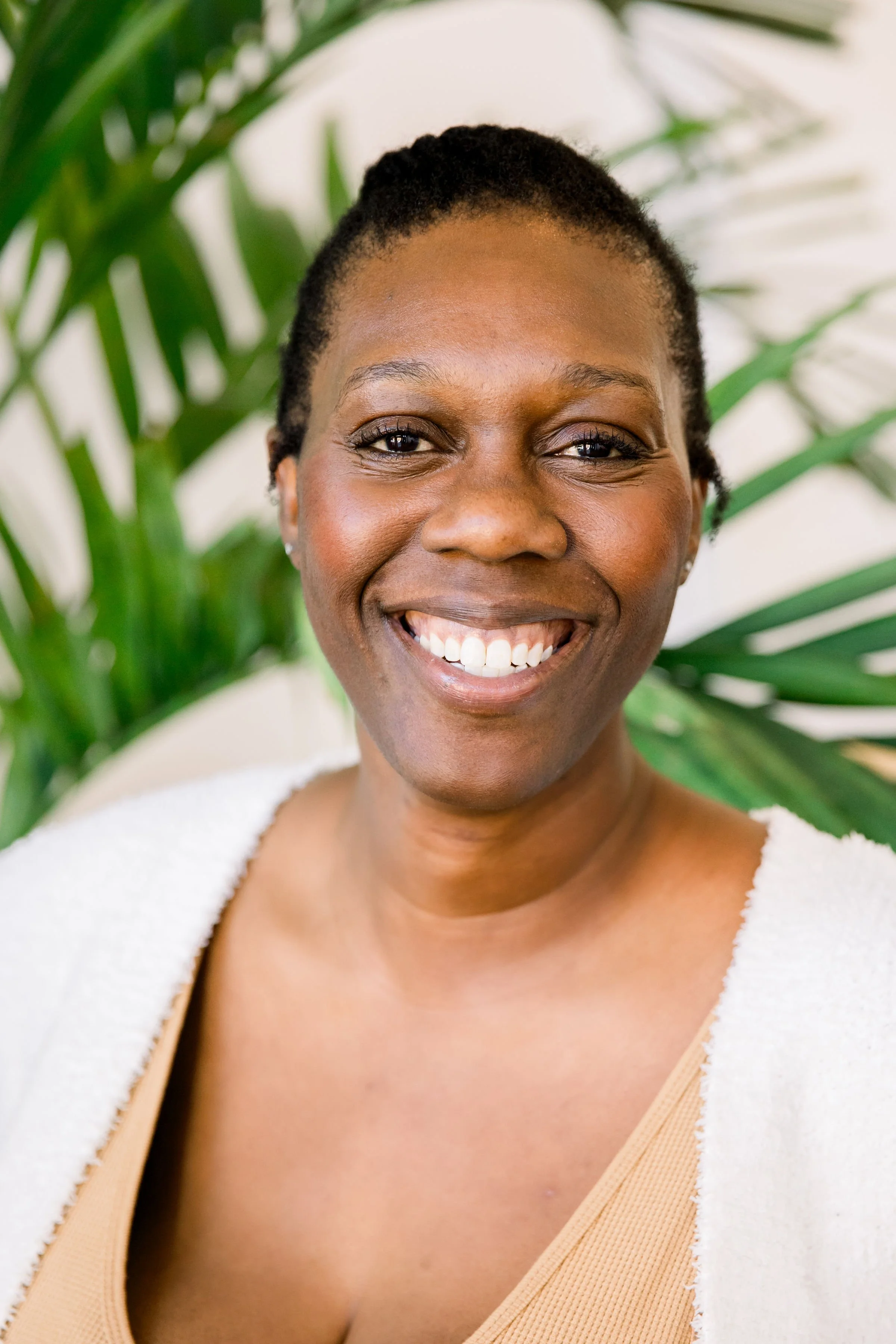 Black woman smiling with green plant behind her