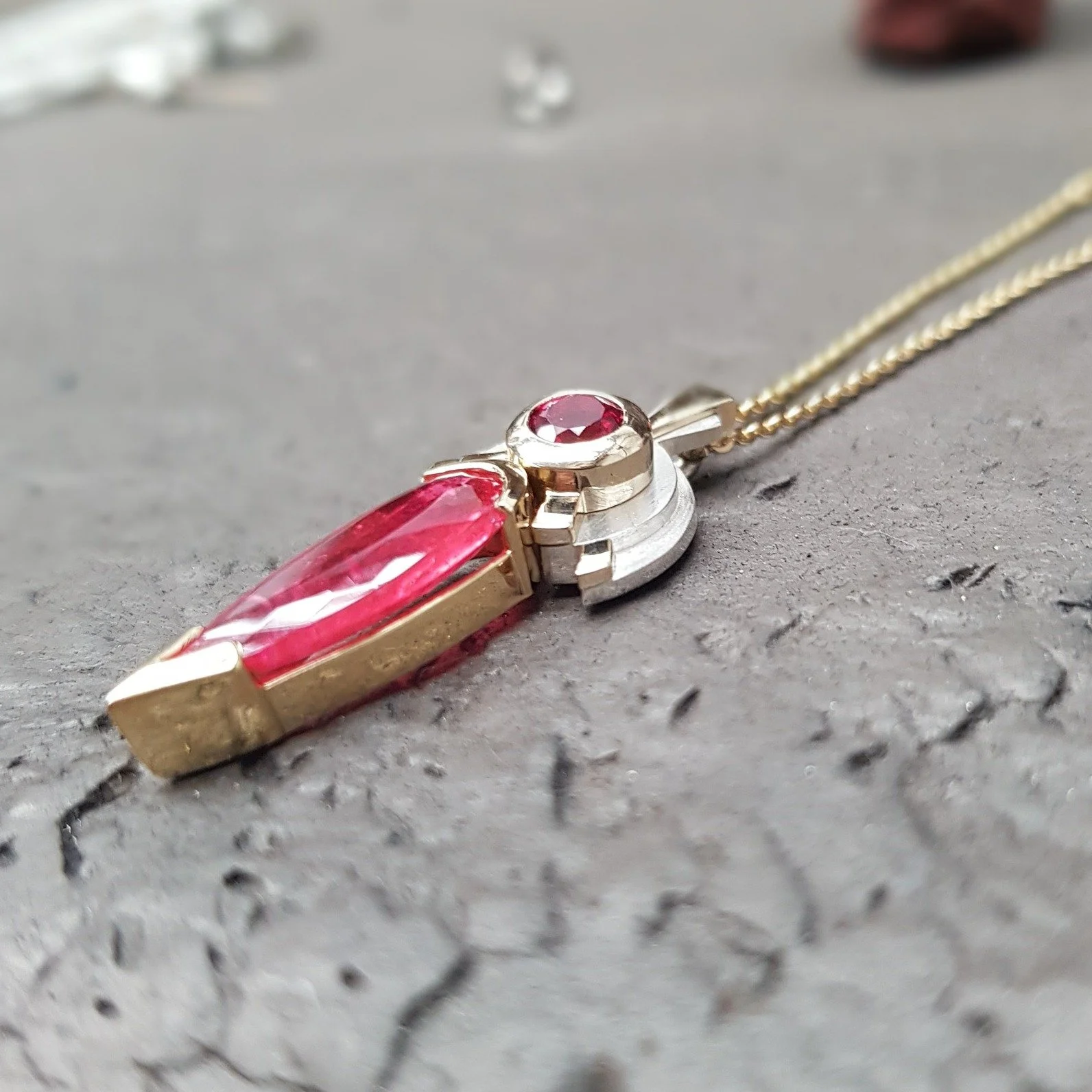 A totally unique, Deco style, two-tone pendant. Set in 18ct yellow gold with a sterling silver stepped backdrop, this pendant features a pink round spinel and elongated pear shaped rhodonite. Amazingly elegant with glorious flashes of colour.

Deco p