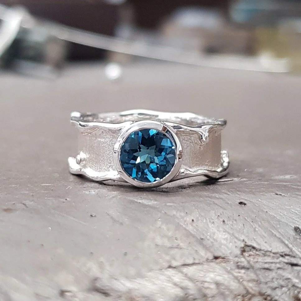 We love the look of molten metal here at SP. This ring is part of our Molten Edge collection which sees drips of solid metal falling from the edges of each piece.  This is a sterling silver ring set with a chequerboard cut London Blue Topaz stone. 

