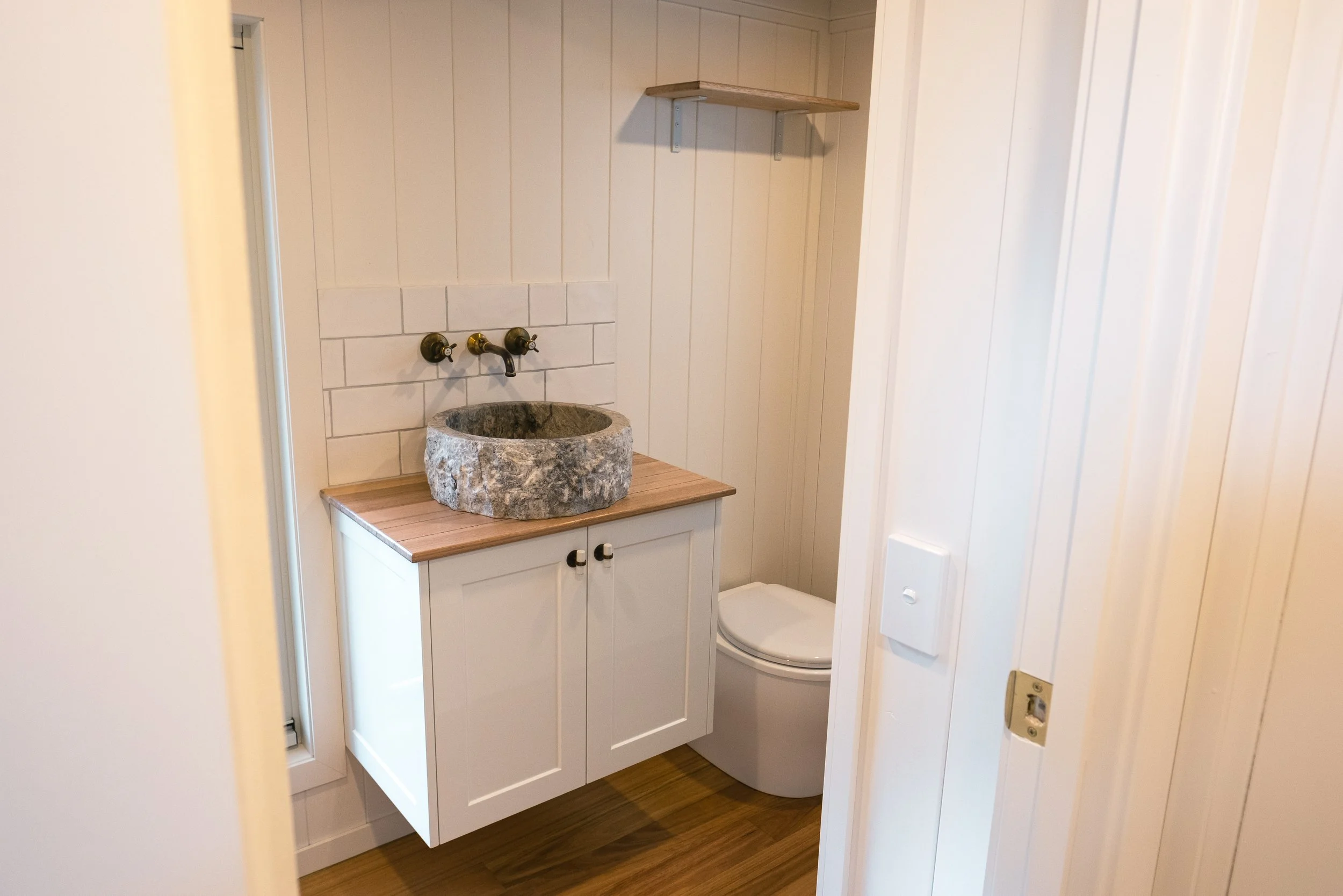 Small bathroom with stone sink, white tiles, and modern fixtures on wood flooring.