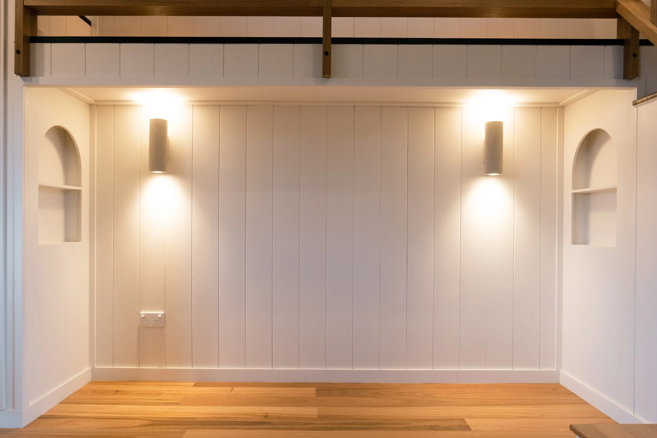 Minimalist alcove with wood flooring, white paneled walls, built-in arches, and wall-mounted lights.