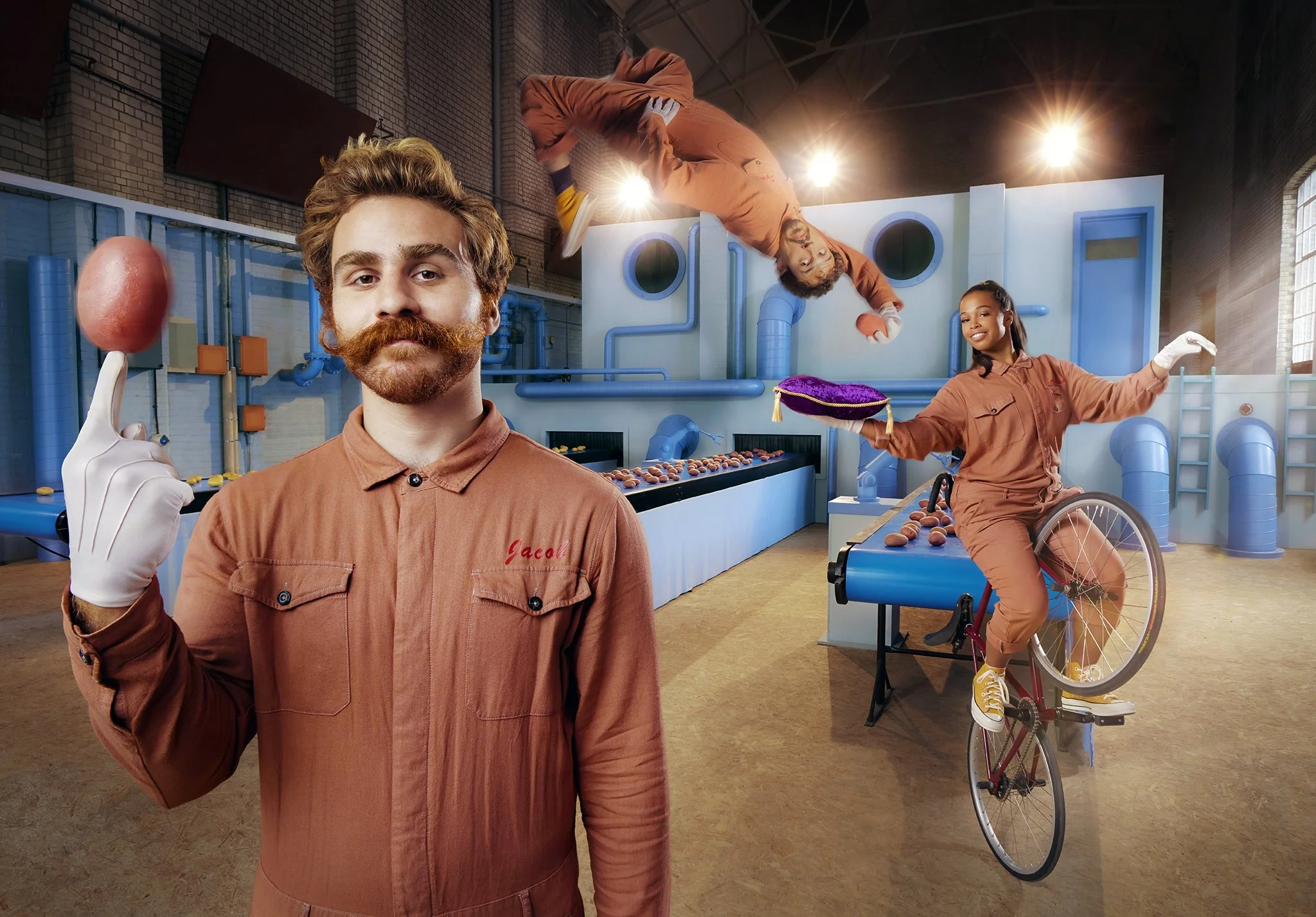 A man with a mustache and beard in the foreground holding a brown egg on his finger, and a woman in a wheelchair performing a wheelie on a bicycle in the background with an indoor activity setup.