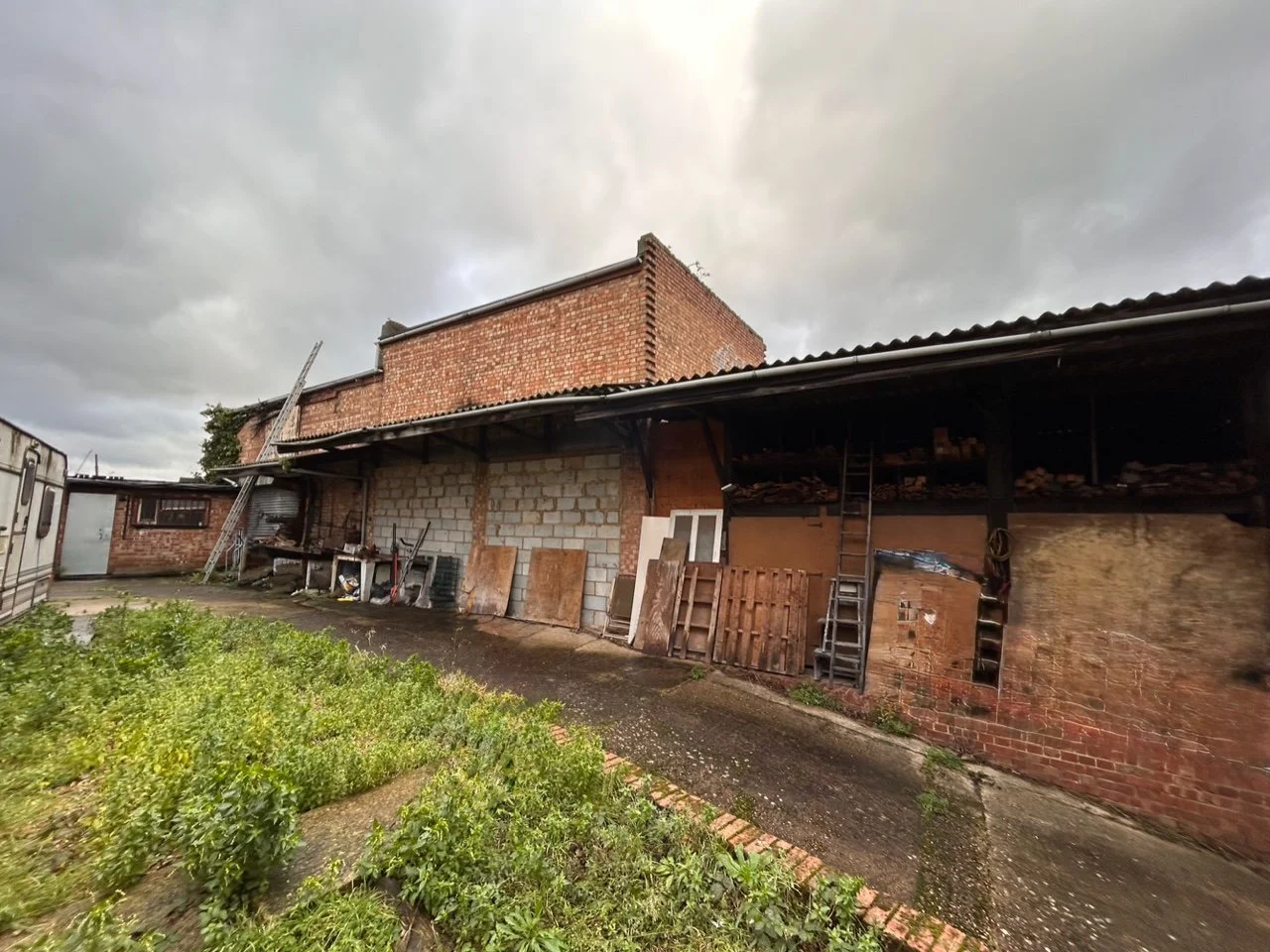 Backyard scene with a brick and cinder block structure, cluttered storage area, and overcast sky.