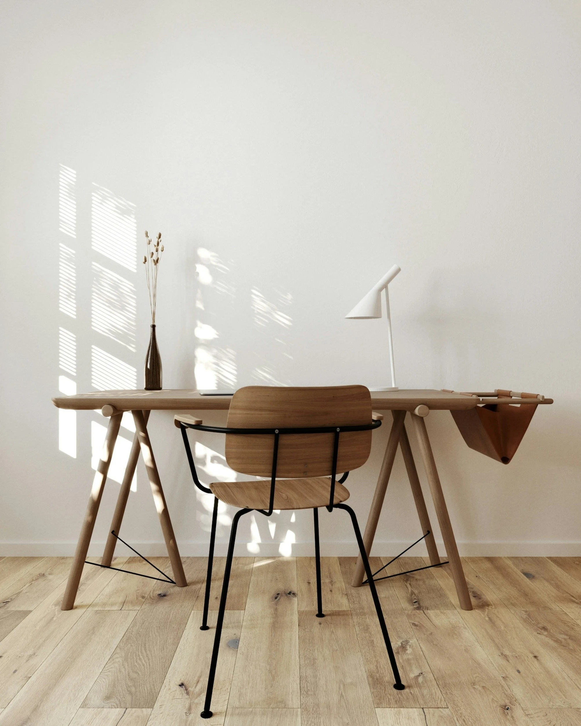 Ein Holz Esstisch mit vier Stühlen in einem Raum mit weißen Wänden. Auf der Tischplatte steht eine weiße Lampe und eine Vase mit trockenen Blumen. Im Hintergrund sind Fenster mit Schattenwurf und eine Holz-Kommode sichtbar.