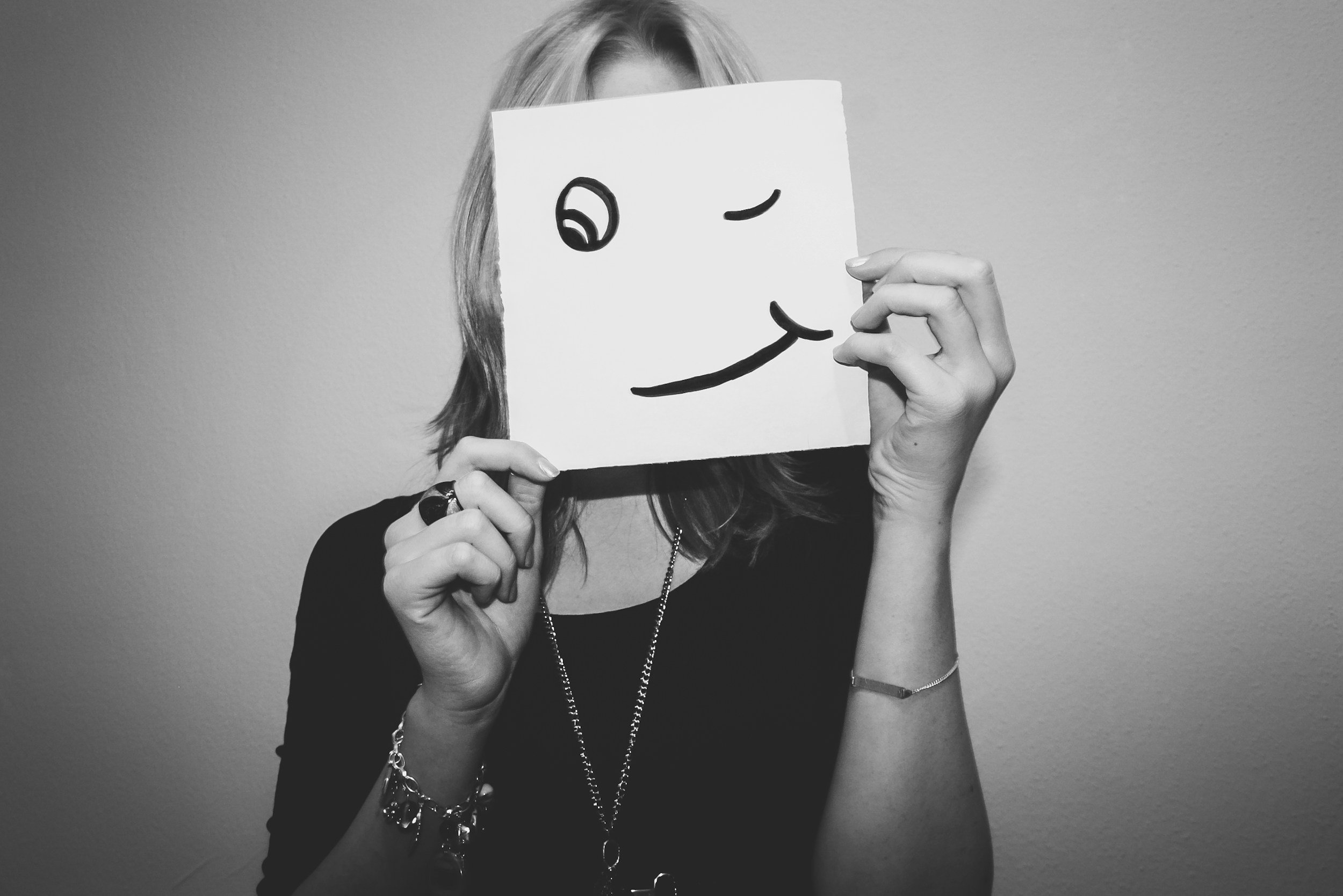 Eine Person hält eine weiße Pullover mit einem lachenden Smiley-Gesicht vor das Gesicht, wodurch nur die Haare und die Hände sichtbar sind.