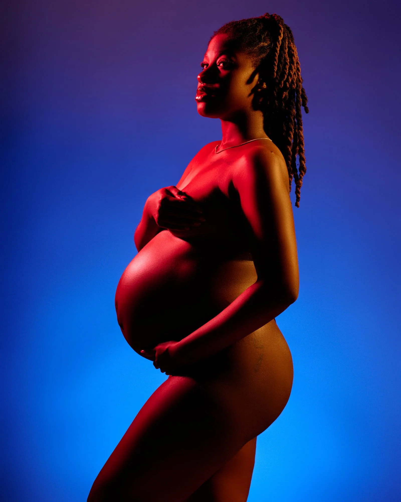 Red and blue gel light sculpting her profile as she cradles the bump.