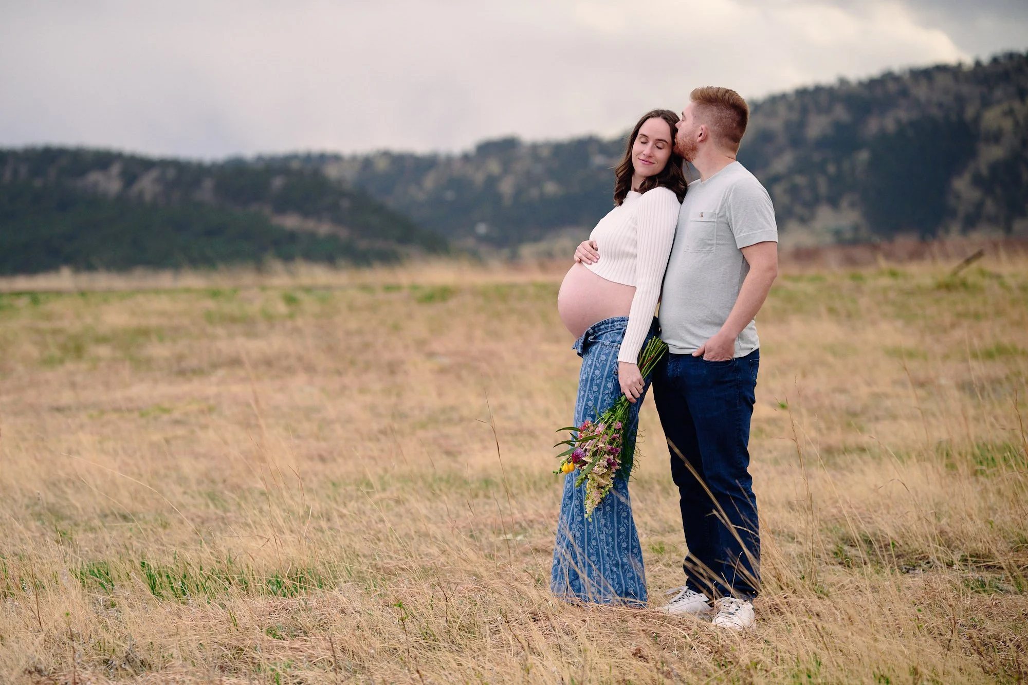 Embroidered denim and fresh-picked wildflowers, tucked under his arm in tall grass.