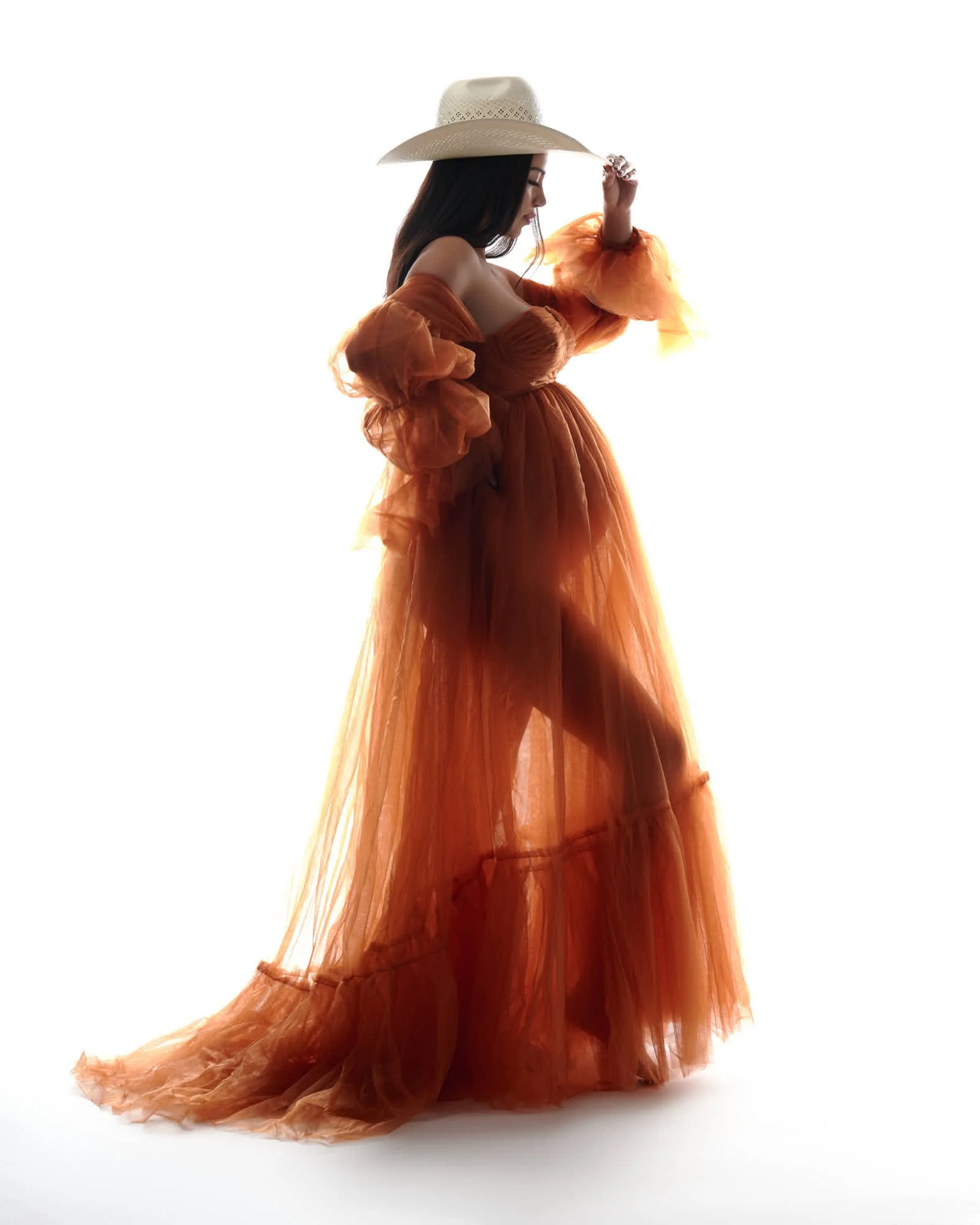Flowing rust tulle gown and a white cowboy hat, glancing back over her shoulder.