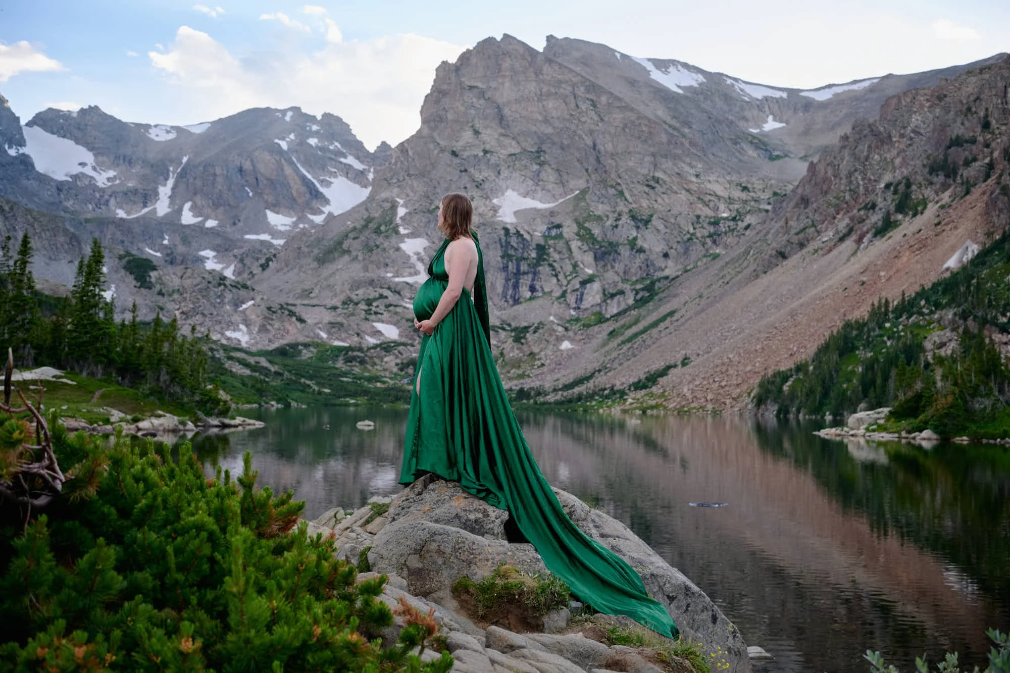 Mountain maternity photoshoot in the Indian Peaks Wilderness with mom standing holding belly in a green parachute dress.