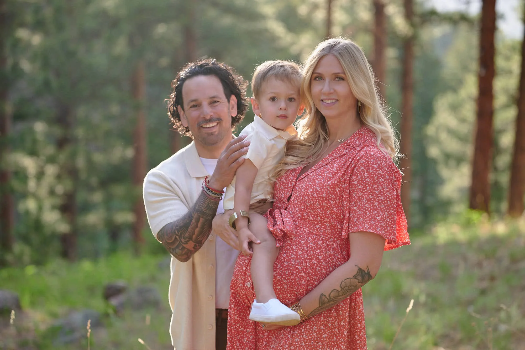 Parents and their toddler close together in warm evening light among the pines.