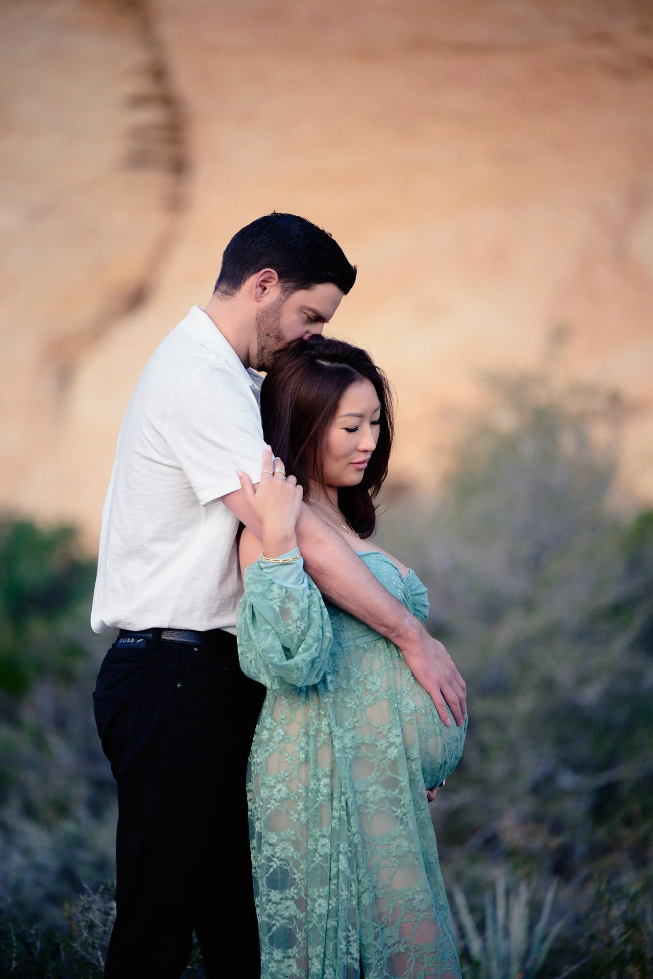 Partner in a white shirt behind her, sage lace gown and desert canyon walls in the sun.