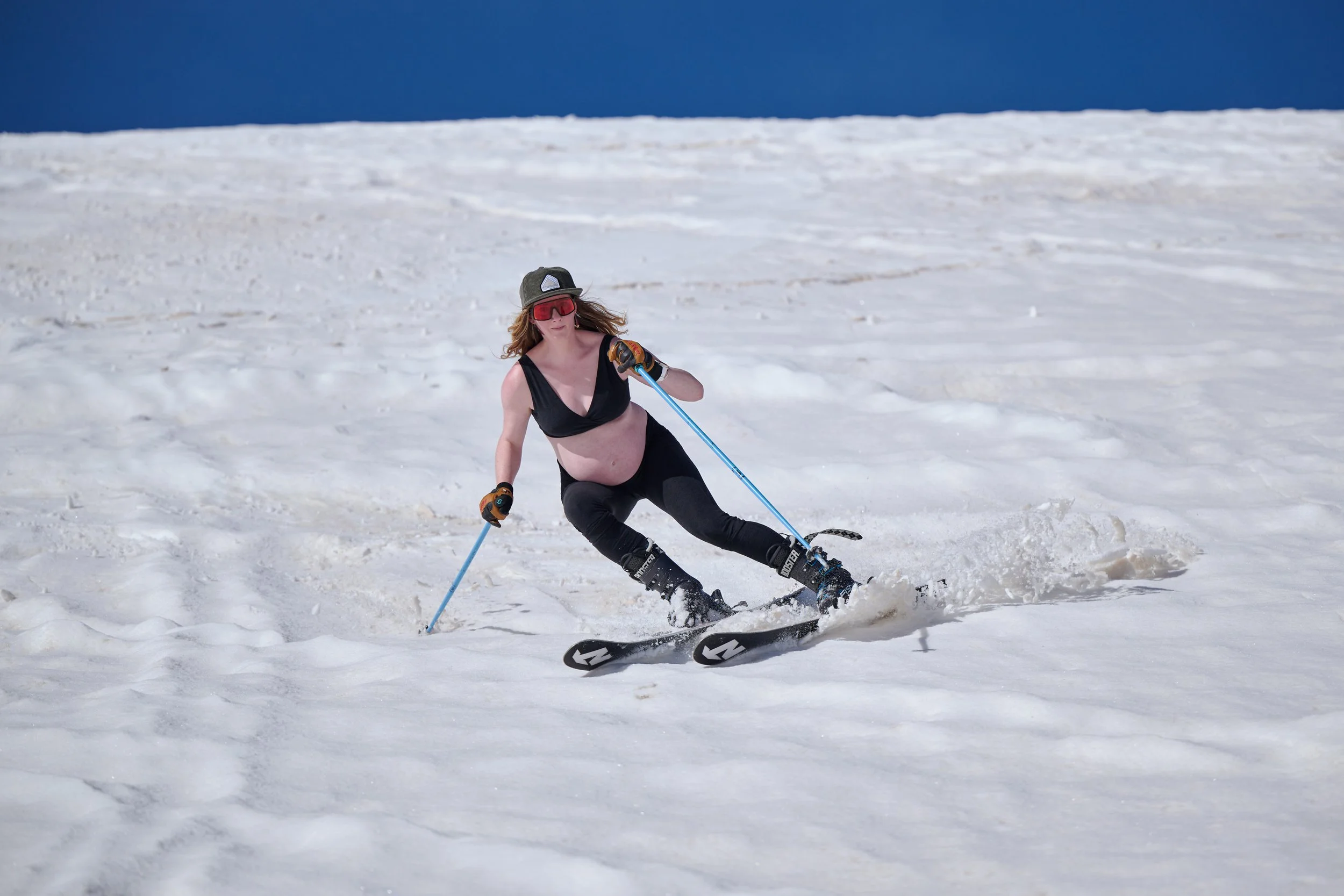 Pregnant skier carving a turn under a bluebird sky.