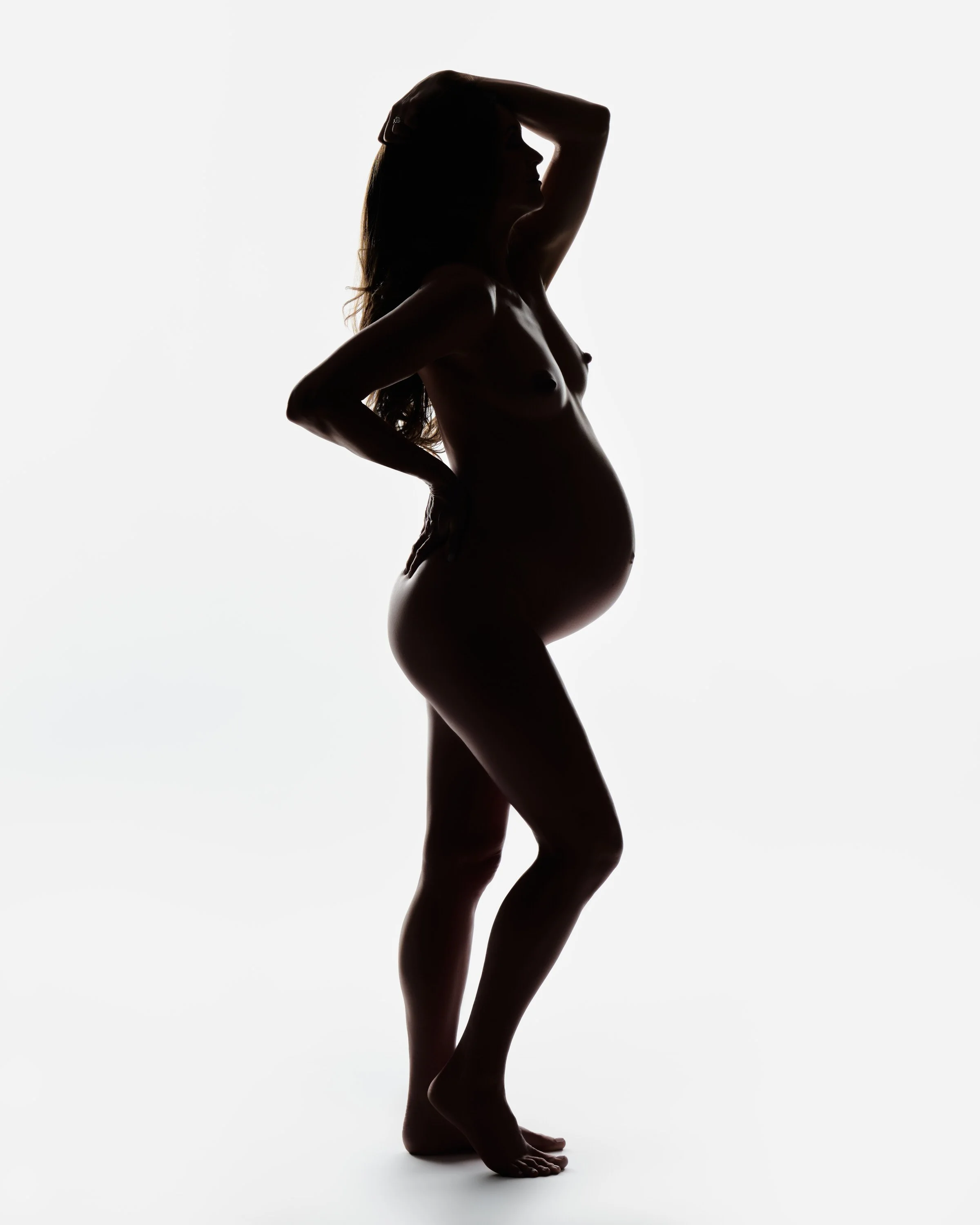 Full length maternity silhouette, the figure dark against a bright studio background.