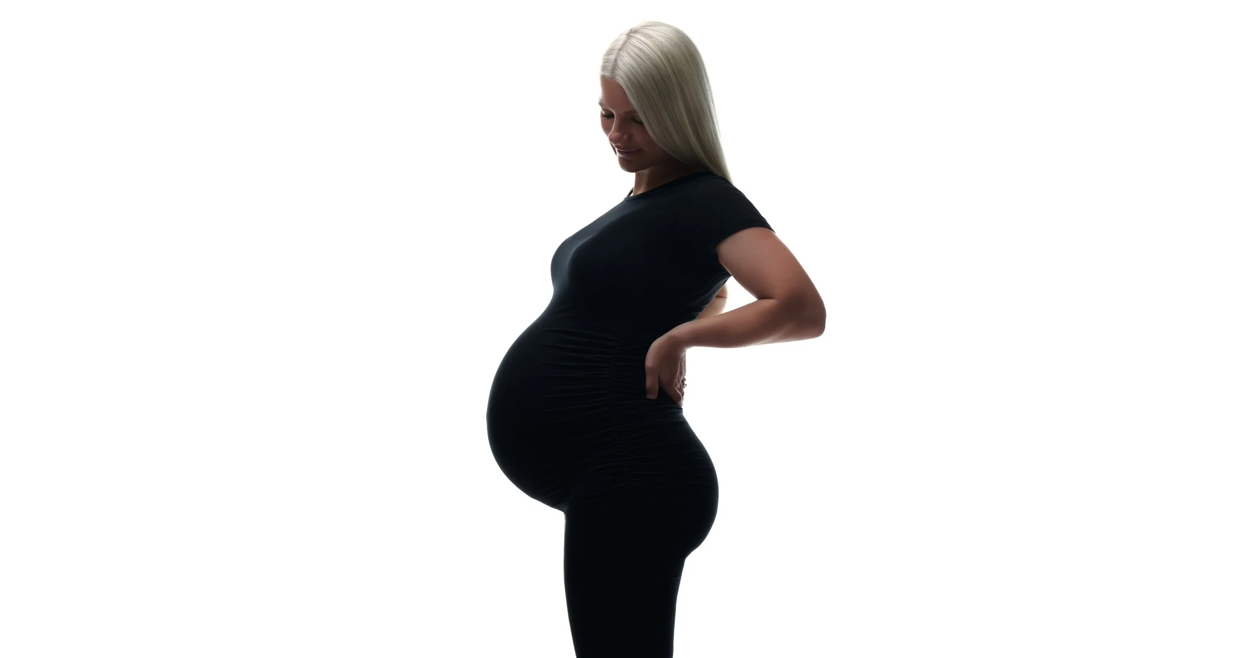 Fitted black dress in full profile, a bright high-key maternity study.