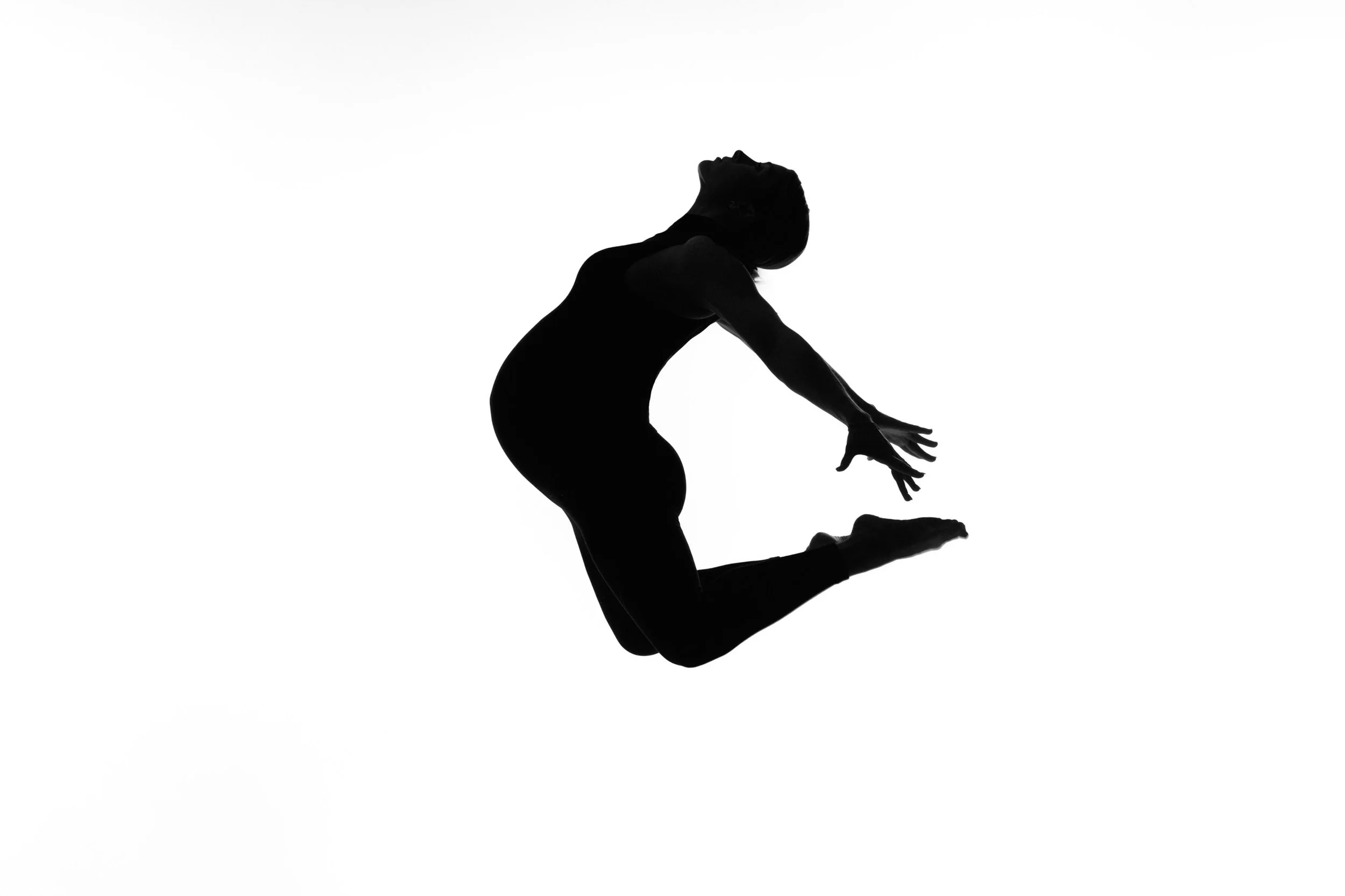 Dancer leaps mid-air in silhouette, head thrown back, a fine art maternity portrait.