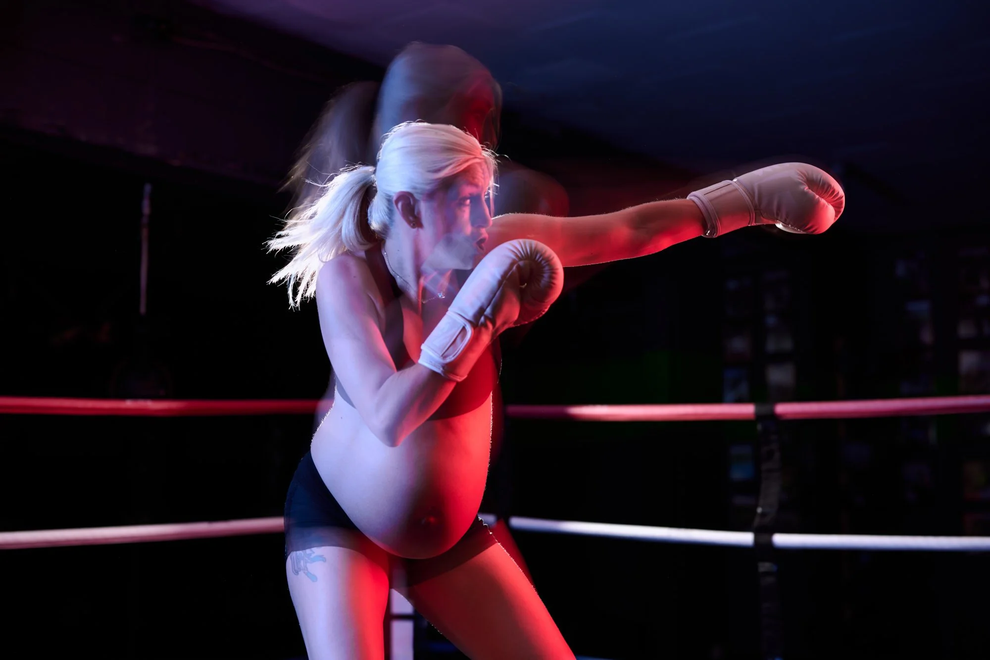 Shadowboxing in the ring under red light, a blur of gloves and a bare bump.