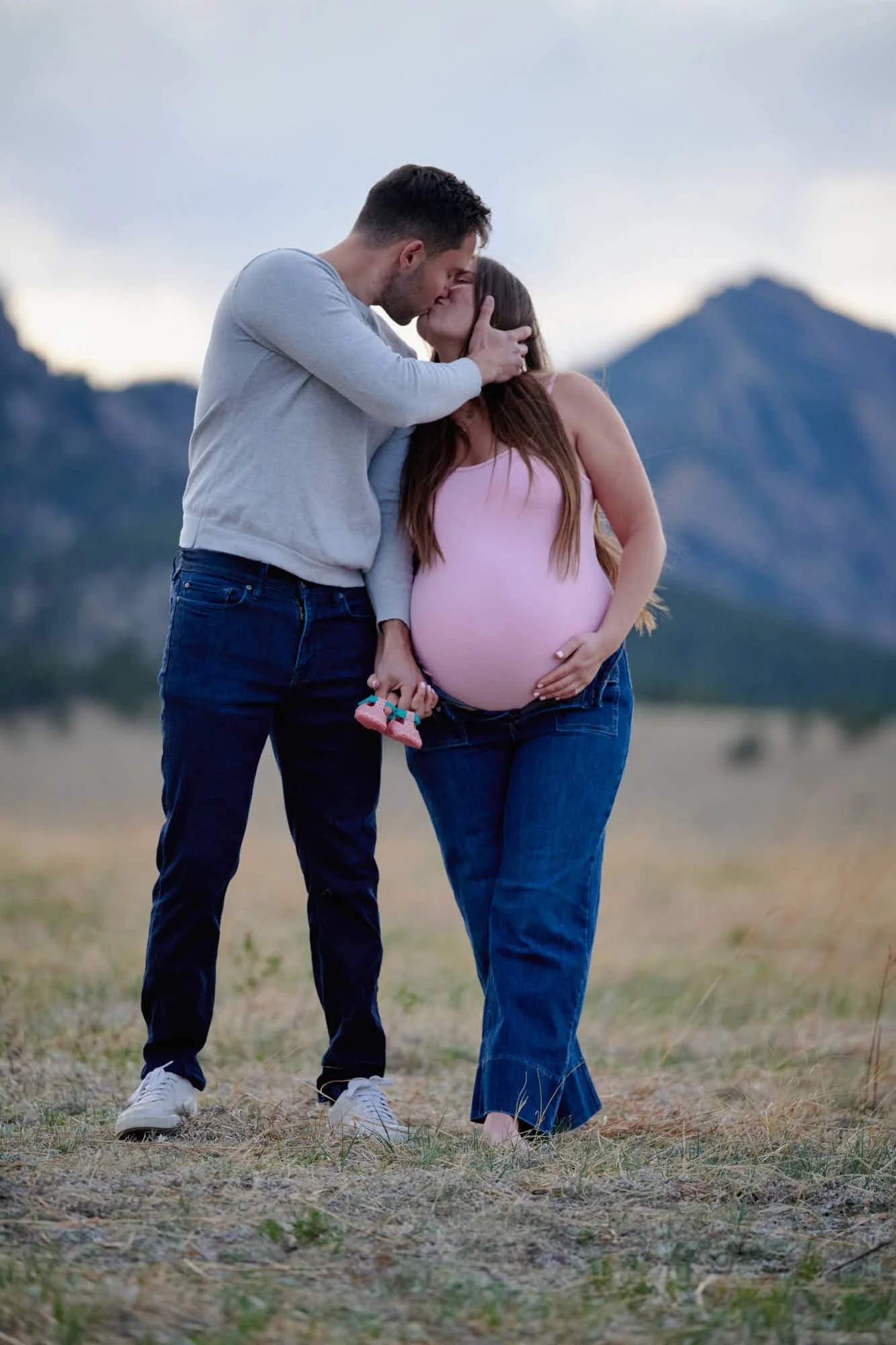 Expecting parents forehead to forehead, holding a pair of tiny shoes between them.