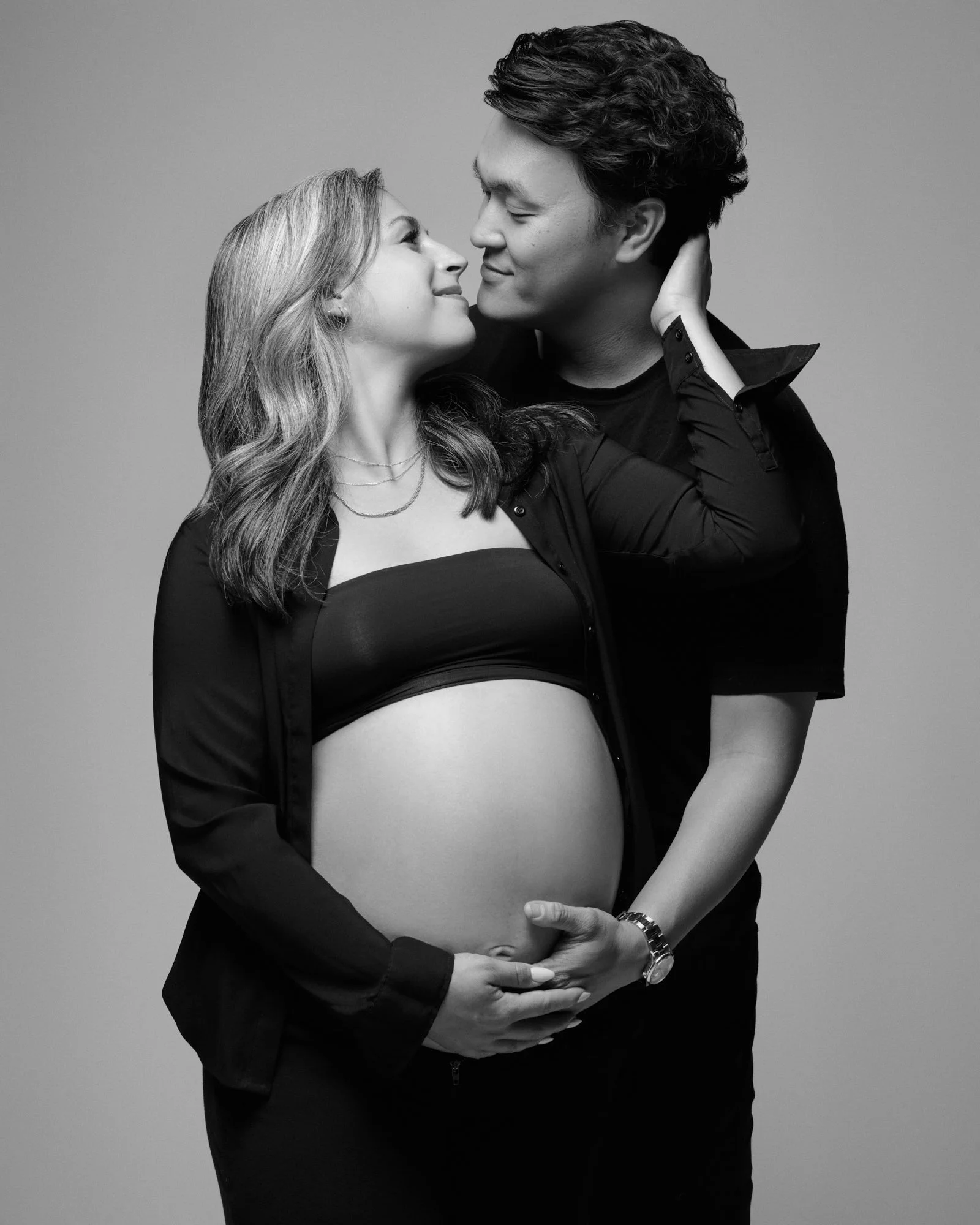 Nose to nose, an expecting couple stacks hands on the baby bump.