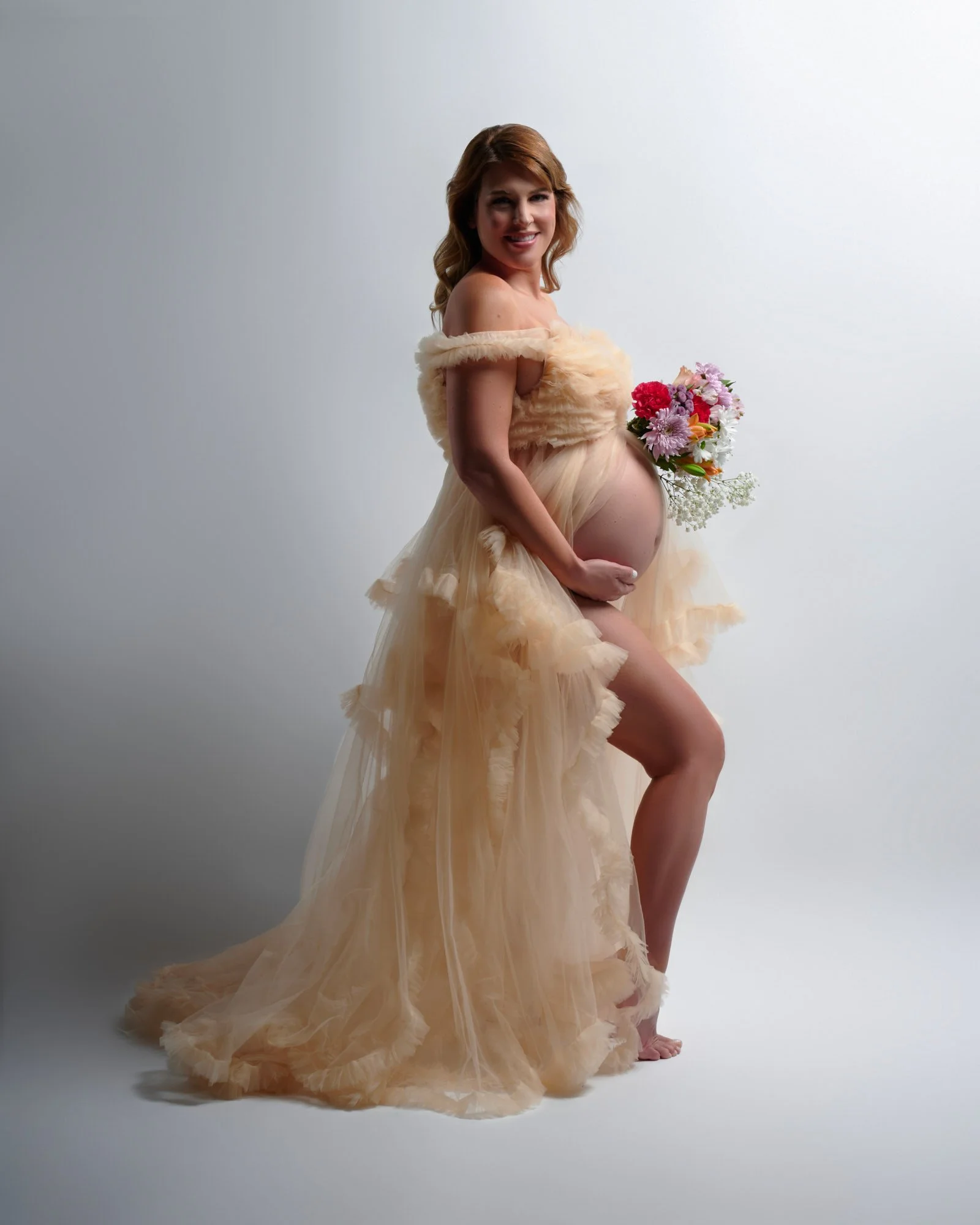 Champagne ruffled tulle gown with a pastel bouquet during a studio maternity session.