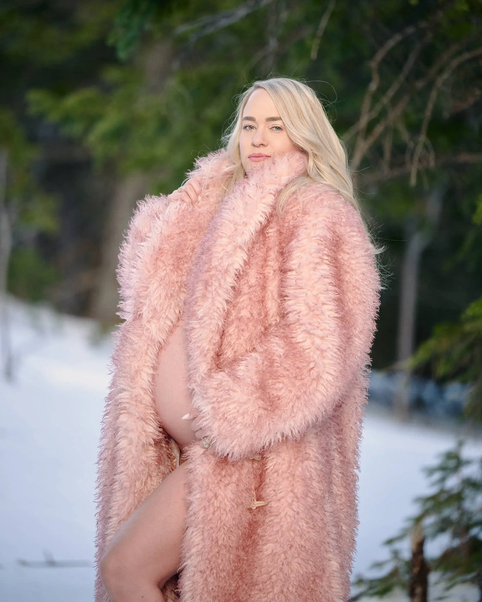 Long pink faux fur coat open over her bump, fresh snow deep beneath the evergreens.