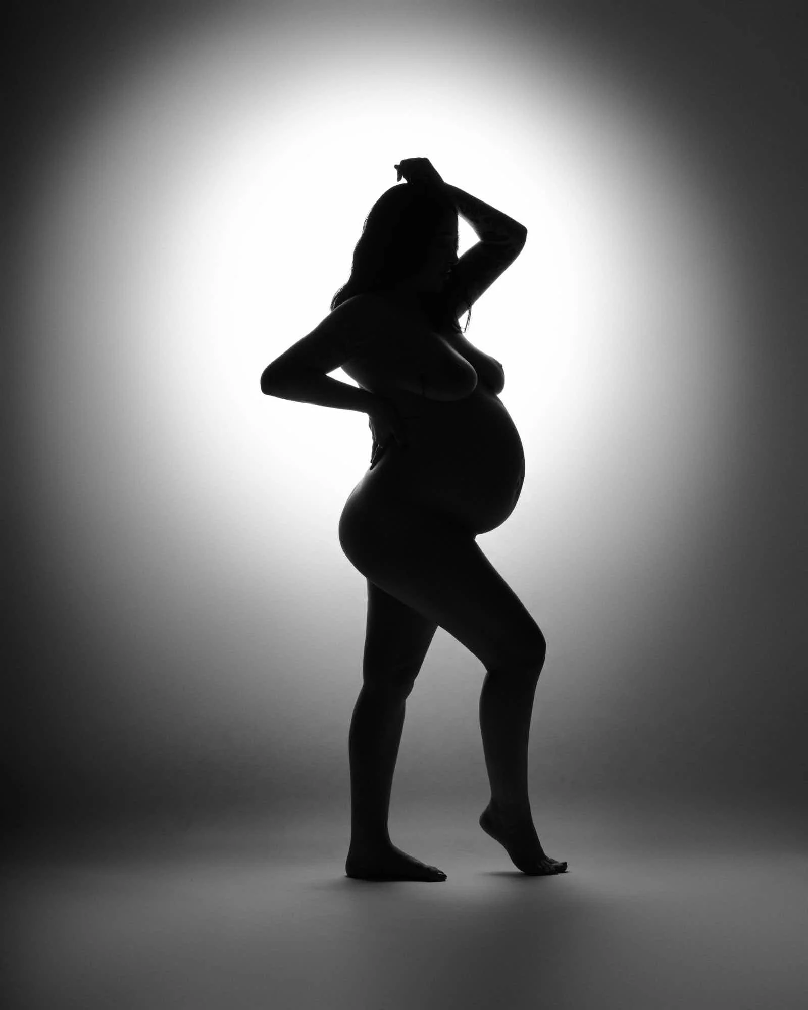 Full silhouette against a bright circle of light, hands lifted to her hair.