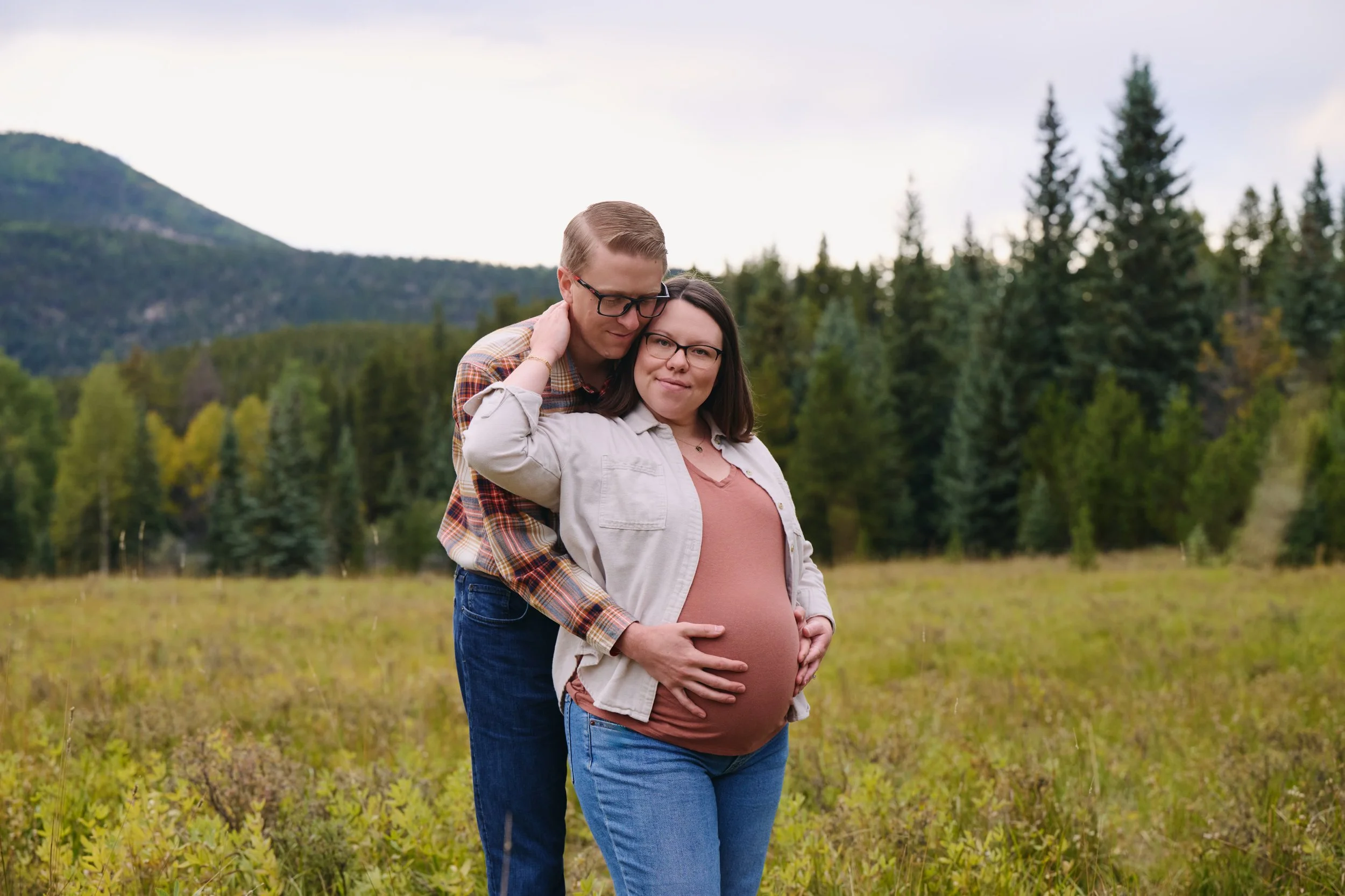 Wrapped from behind in a high mountain meadow, plaid flannel and a quiet evergreen backdrop.