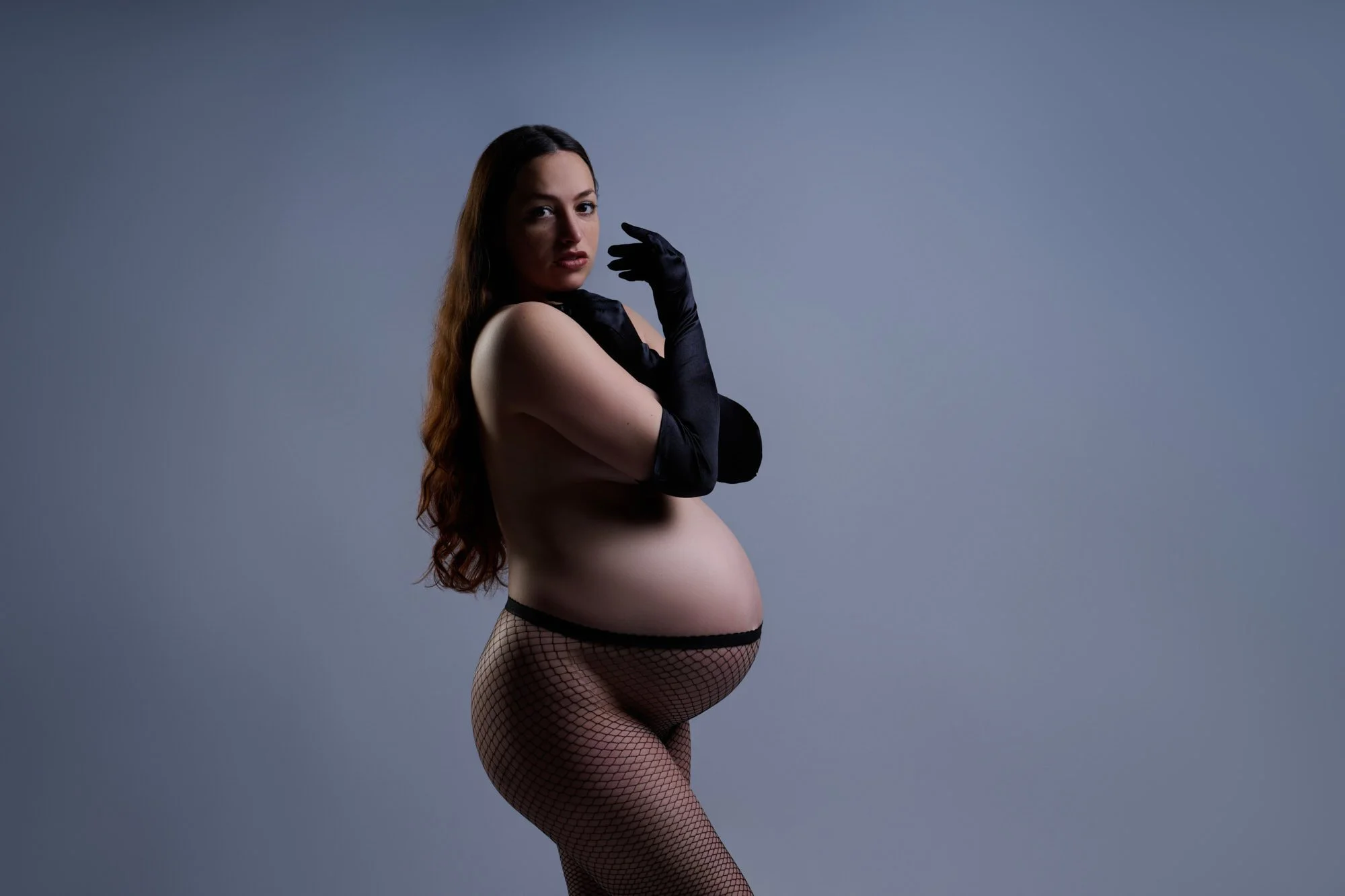Long opera gloves and fishnets against soft grey, chin tipped toward her shoulder.
